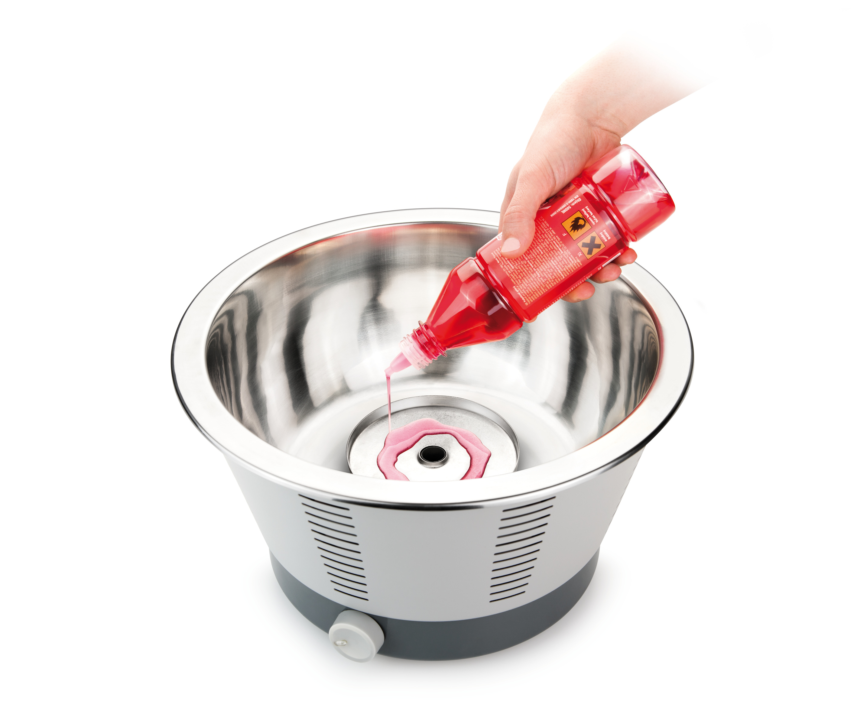 Eine Hand gießt rosa Flüssigkeit aus einer roten Flasche in eine Zuckerwattemaschine aus Edelstahl.