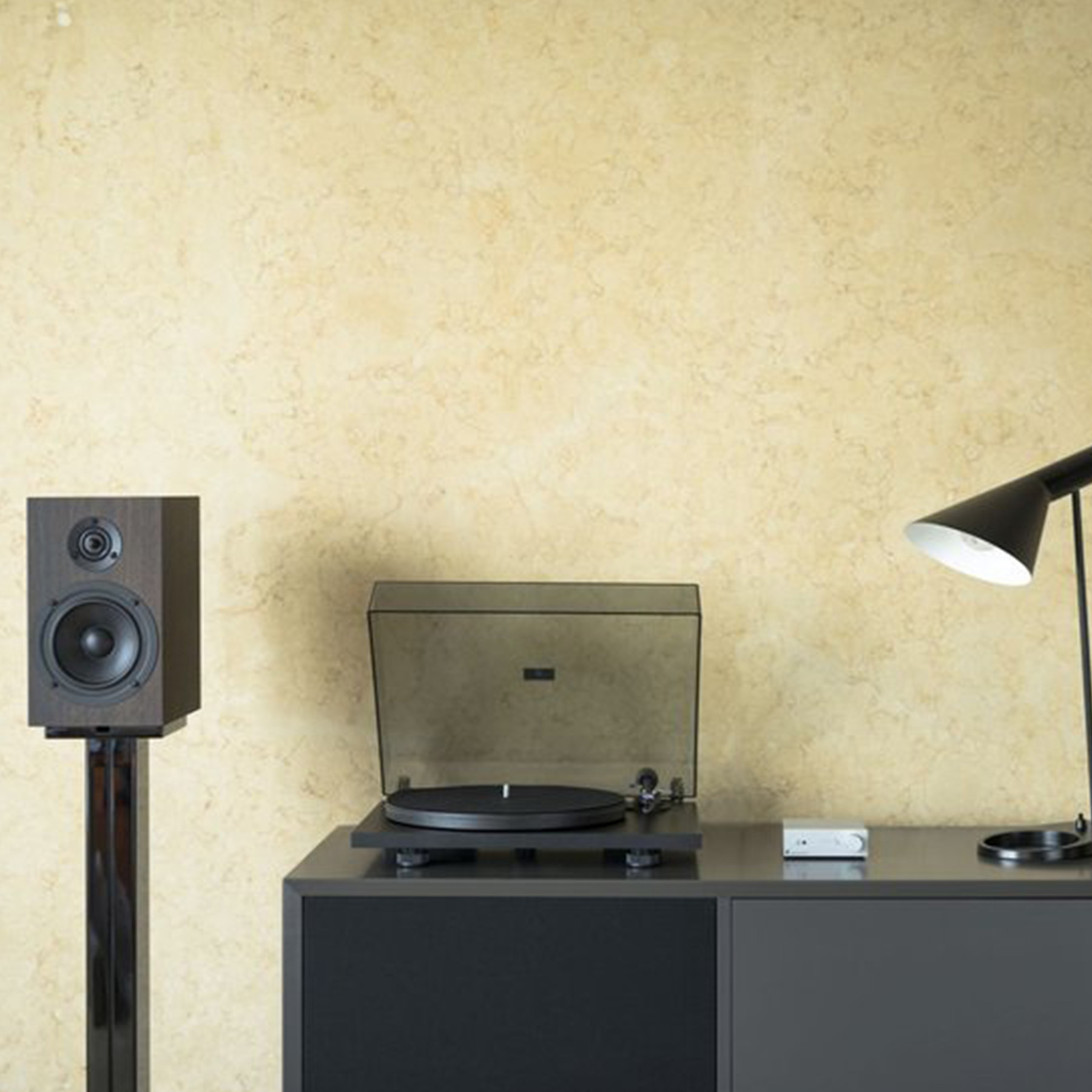 Giradischi su un mobile con altoparlante e lampada. Sfondo muro beige.