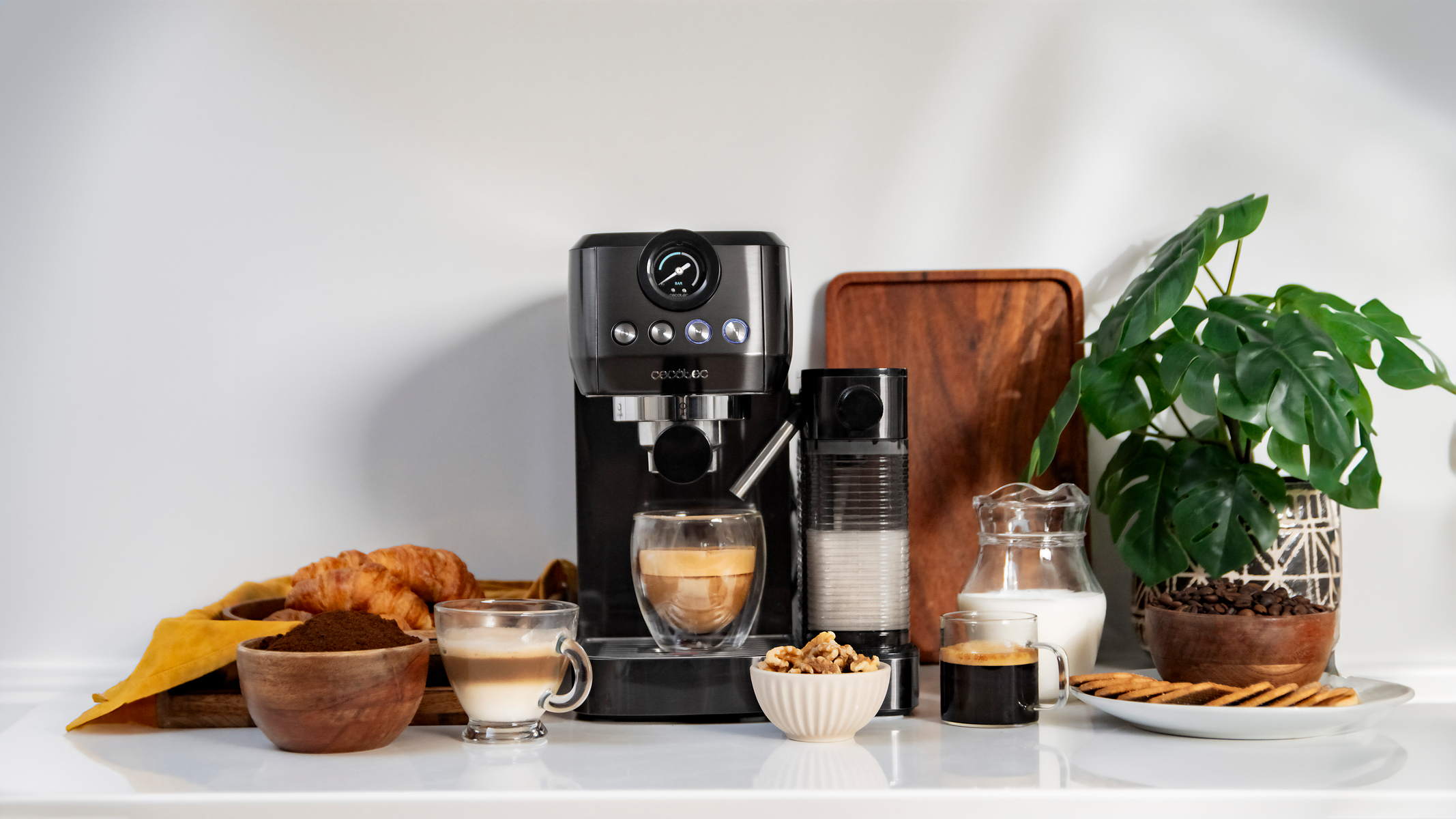 Una máquina de espresso con tazas de café, jarra de leche, pasteles y otros artículos para el desayuno.