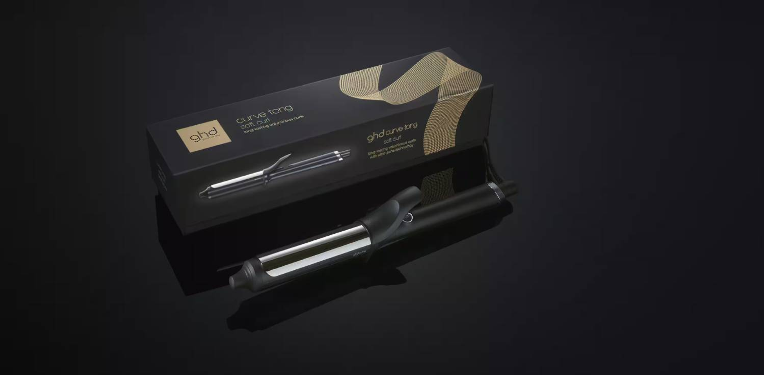 GHD Curve Tong im Karton. Schwarzer Lockenstab mit goldenen Akzenten, der auf einer dunklen, reflektierenden Oberfläche liegt.