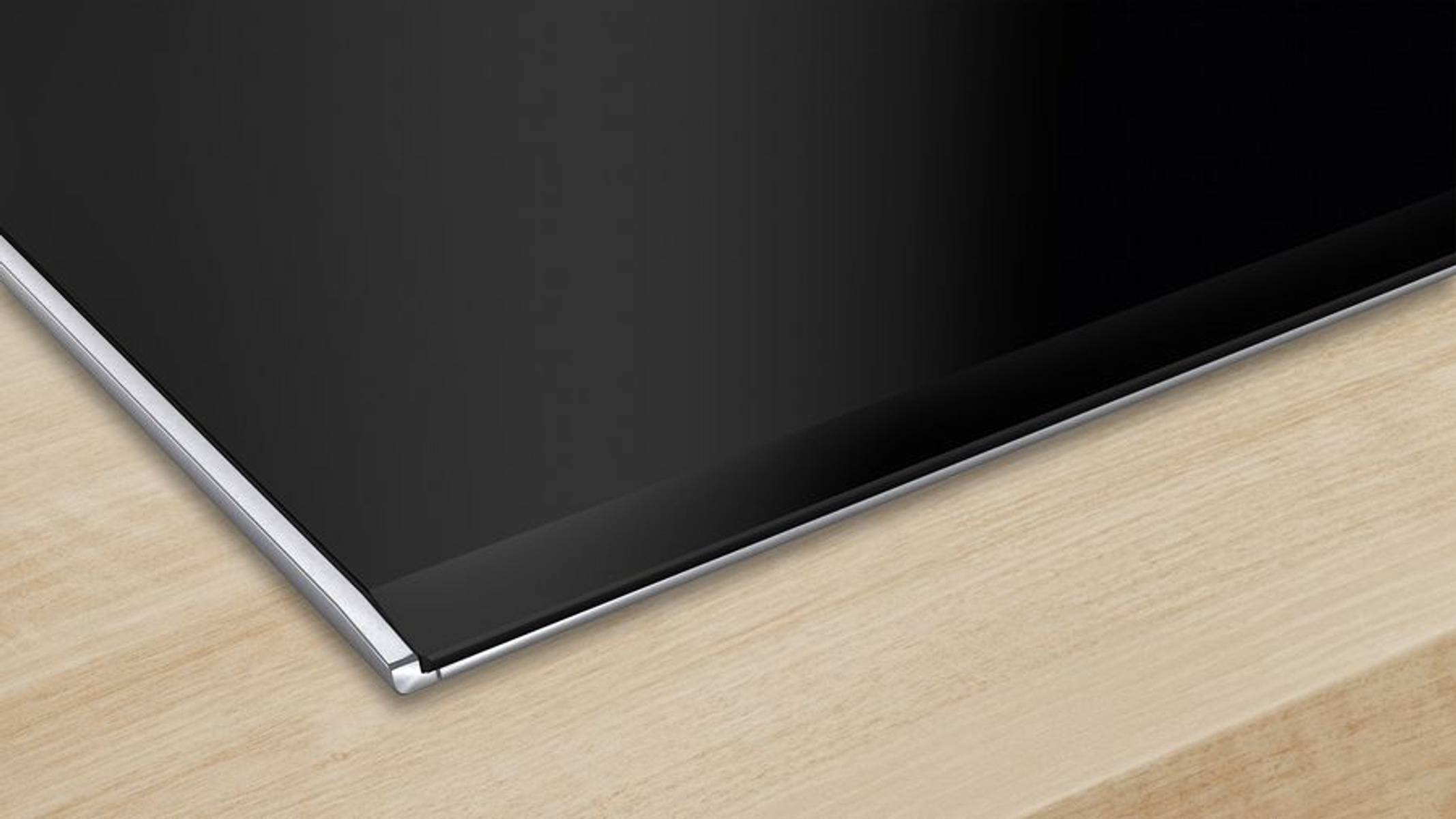 Zbliżenie czarnej płyty kuchennej ze srebrną obwódką na jasnym drewnianym blacie.