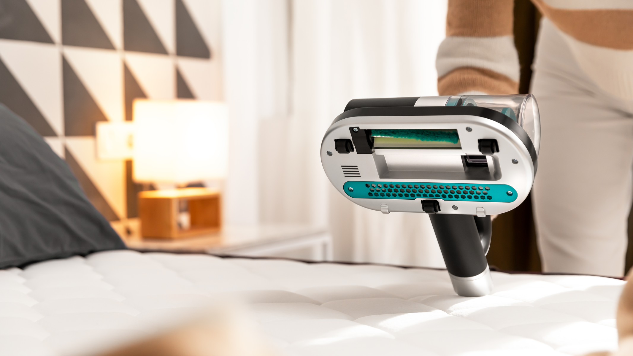 Odkurzacz z przedłużonym uchwytem umieszczony na materacu. W pobliżu jest osoba.