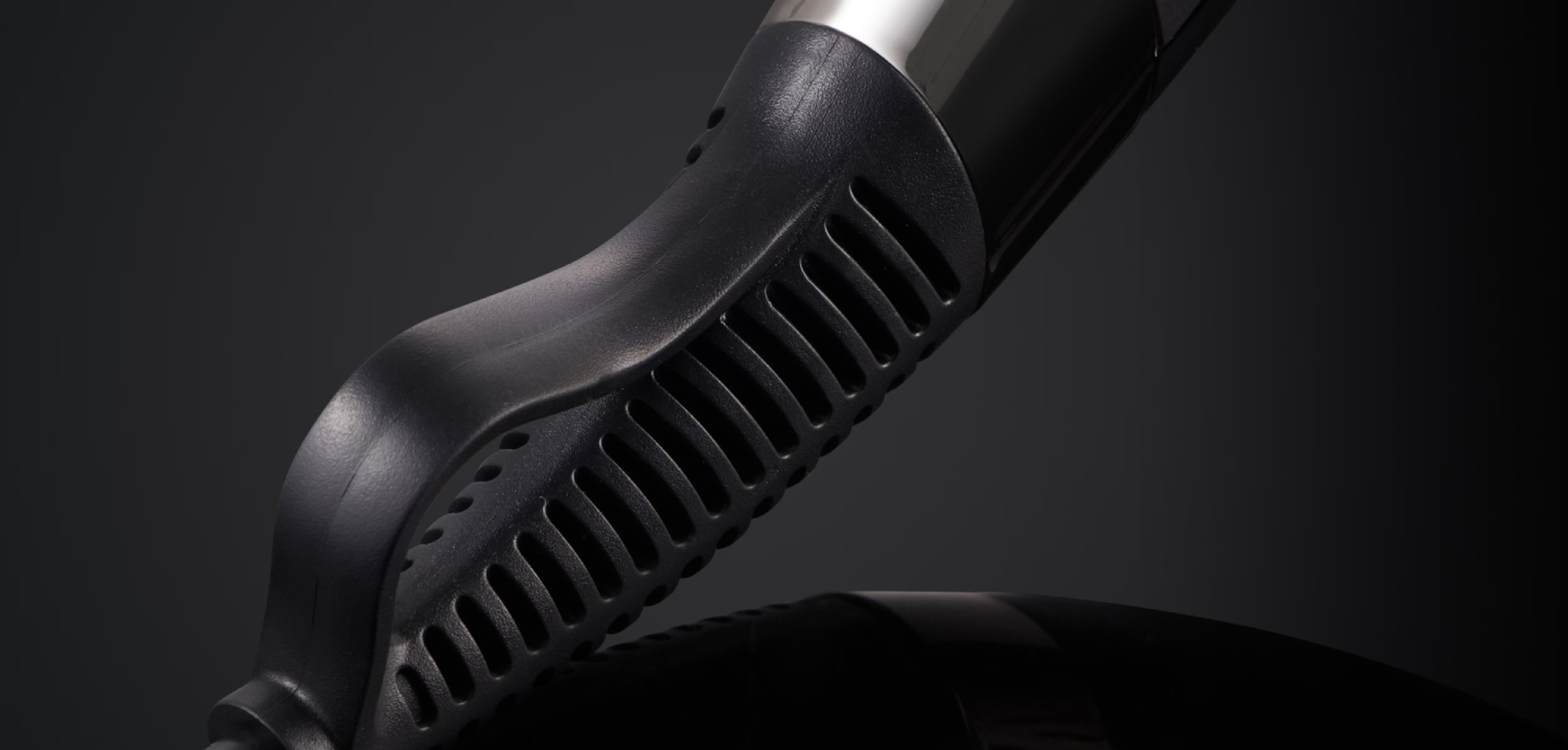 Primer plano del mango de un secador de pelo negro. El mango tiene un diseño ergonómico y texturizado.