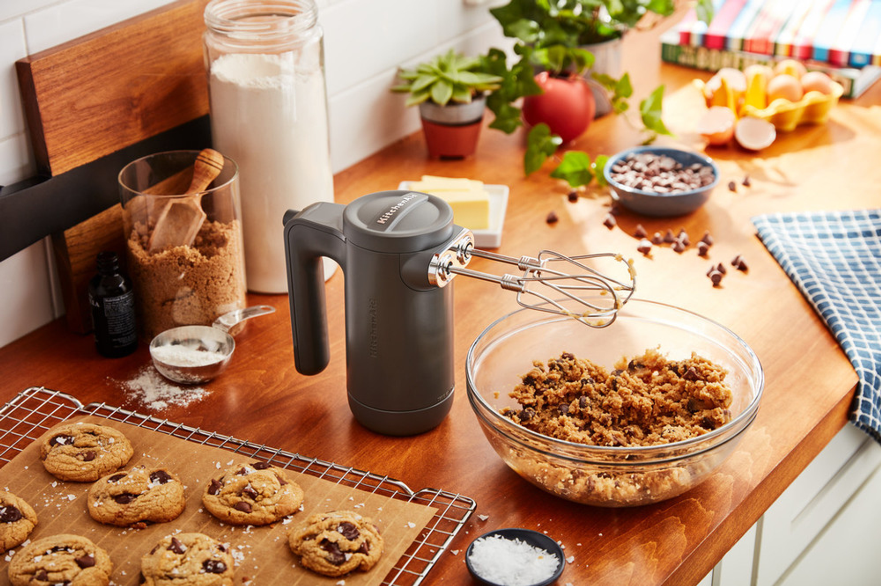 Bir kapta kurabiye hamuru olan KitchenAid el mikseri. Şeker ve tereyağı gibi malzemeler görünür.
