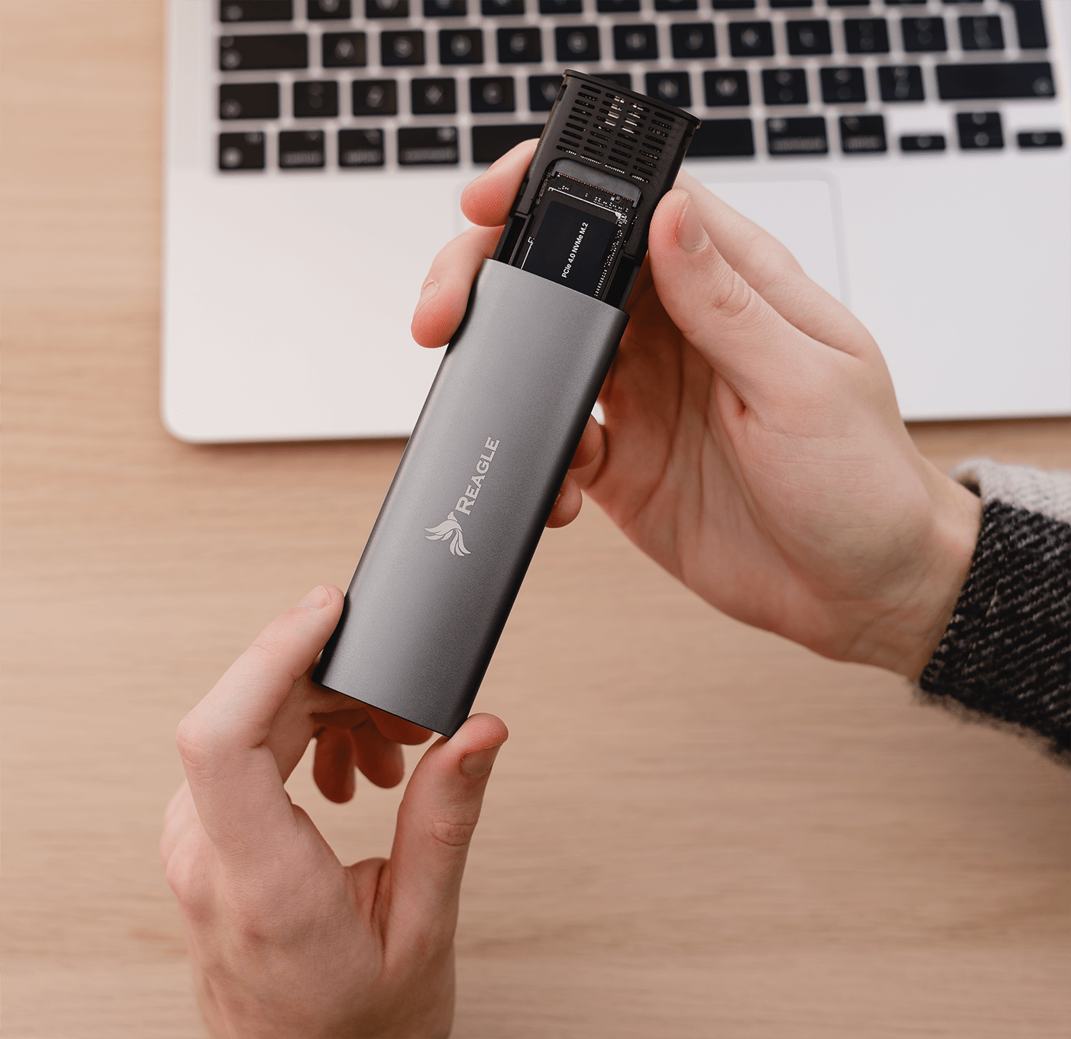 Dłonie trzymają srebrną obudowę zewnętrznego dysku SSD z PCBA nad laptopem.