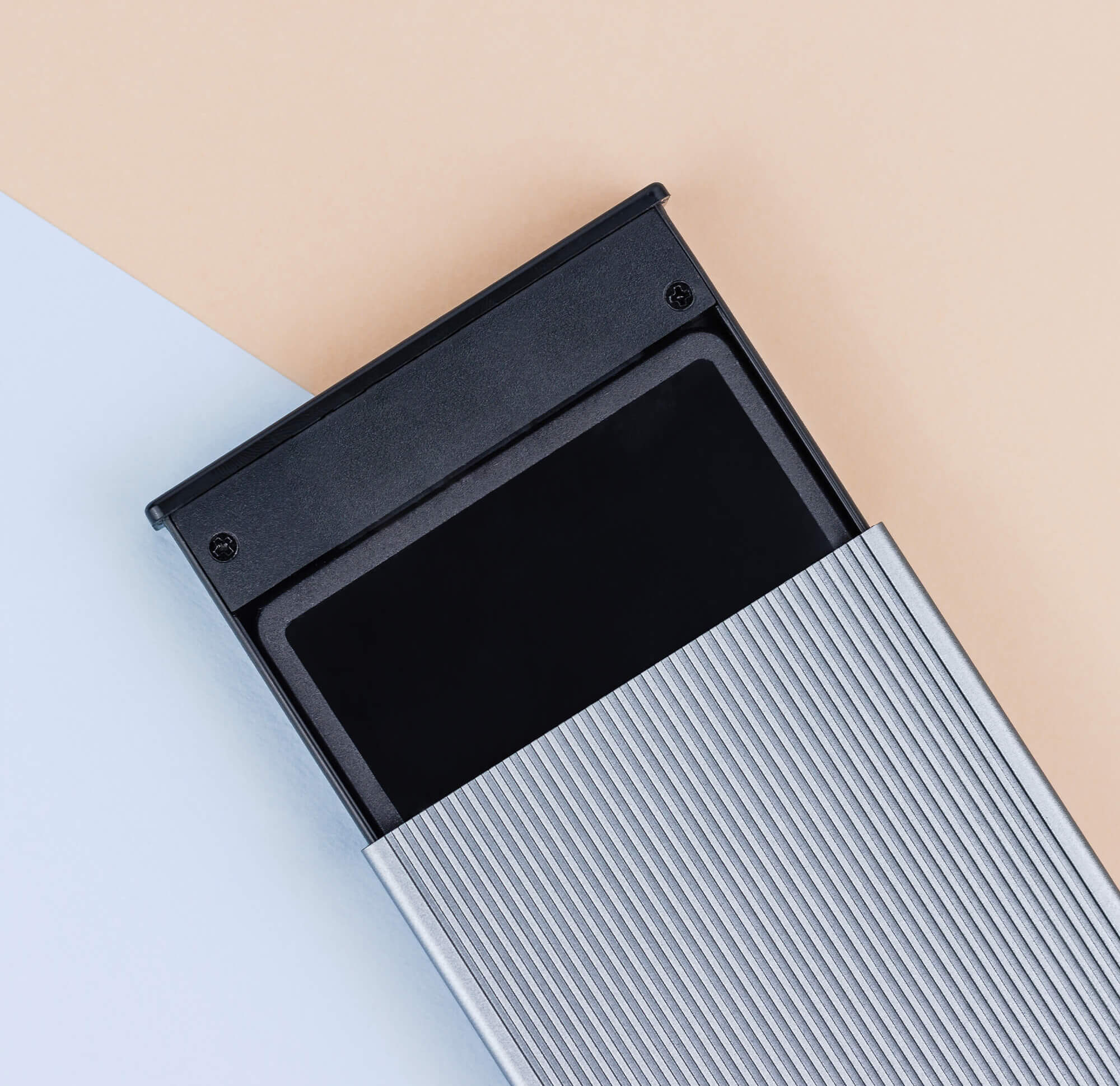 Srebrne i czarne urządzenie, prawdopodobnie dysk twardy lub pamięć zewnętrzna. Ukośnie na jasnym tle.