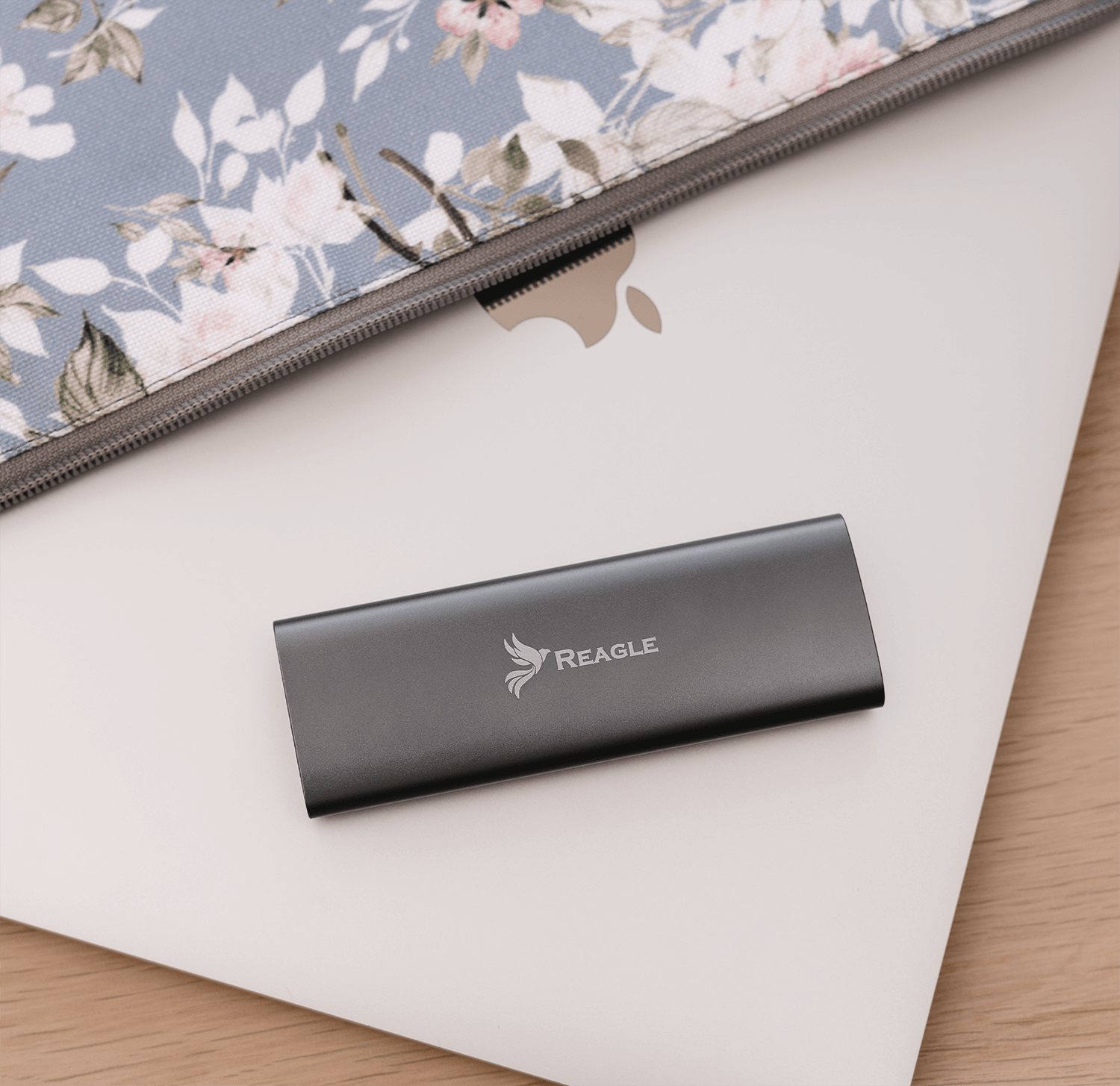 Szary zewnętrzny dysk twardy REAGLE na białym laptopie Apple. Kwiatowy futerał w tle.