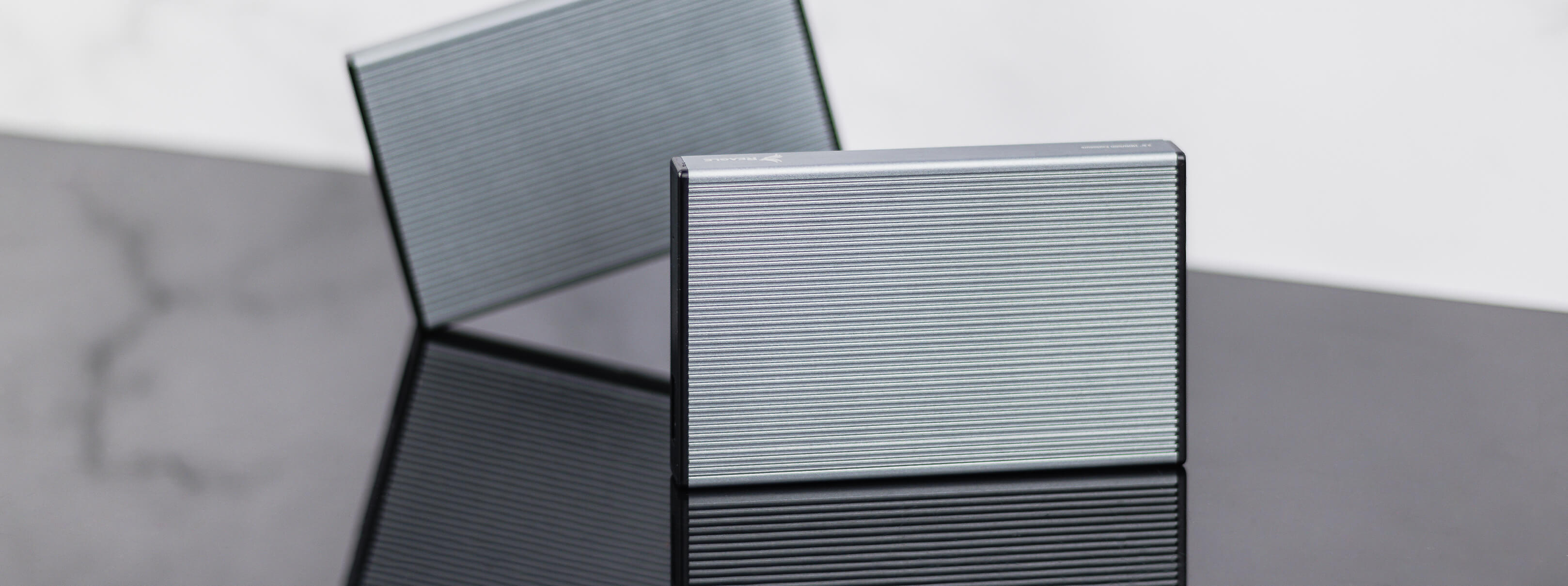 Dwa srebrne, prostokątne etui na karty. Odbijają się na błyszczącej, czarnej powierzchni.