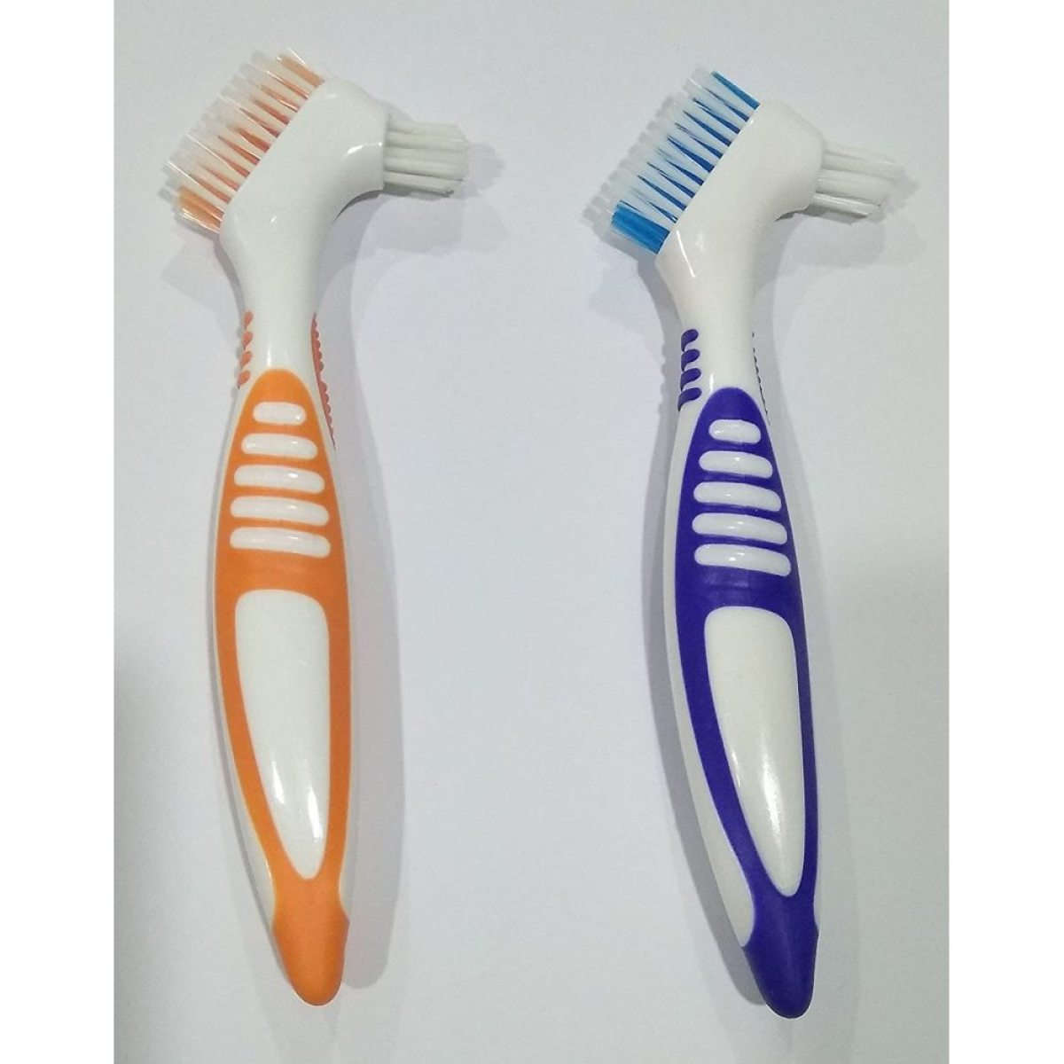 Zwei weiße und bunte Zahnbürsten für Zahnprothesen, orangefarbene und blaue Griffe mit Borsten.