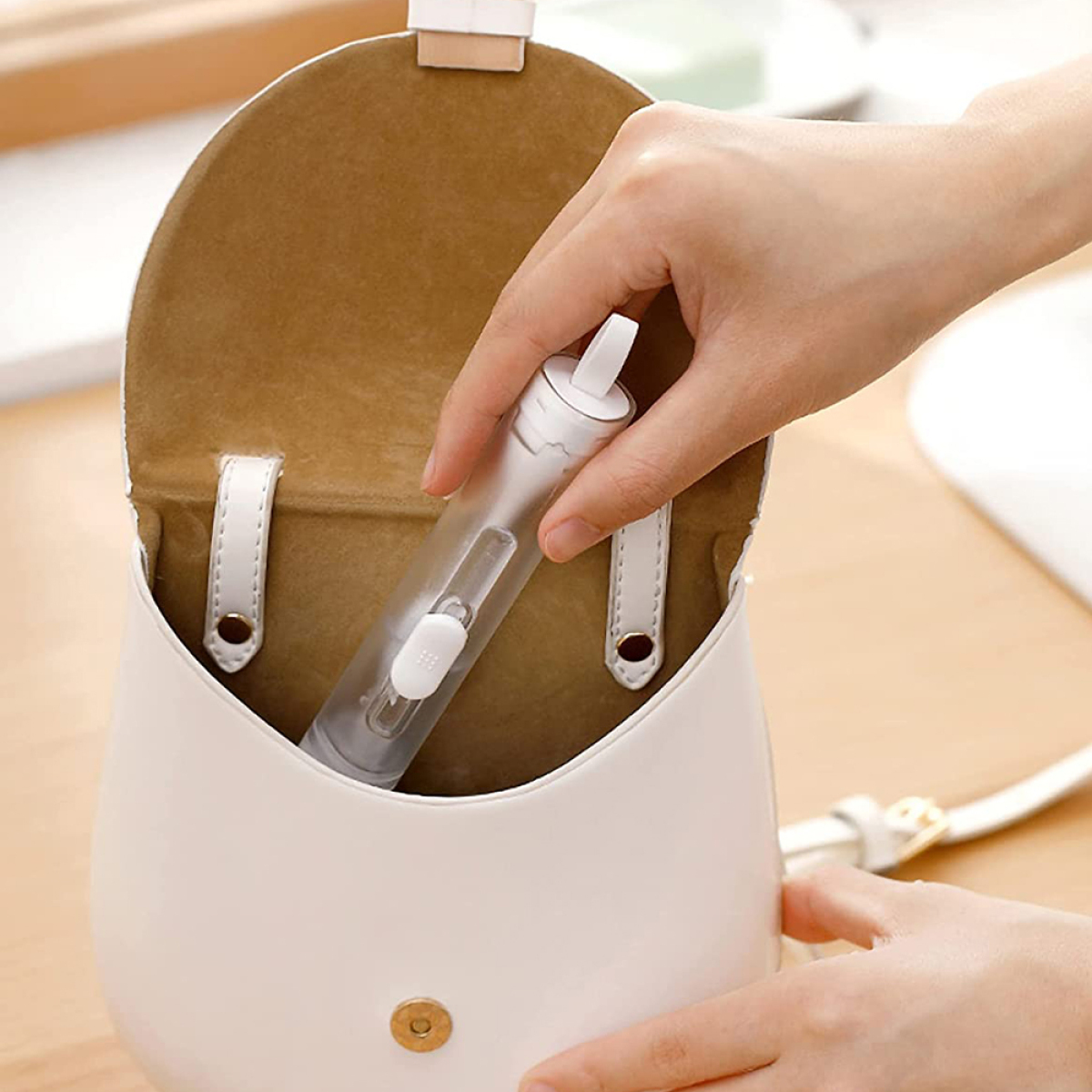 Eine Hand greift in eine weiße Handtasche, um eine transparente, zylindrische Wasserflasche herauszuziehen.