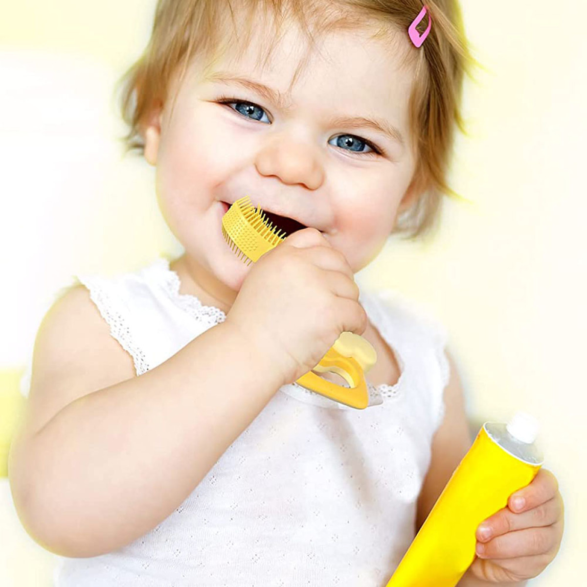 Ein Baby lächelt, hält eine gelbe Beißbürste und gelbe Zahnpasta.