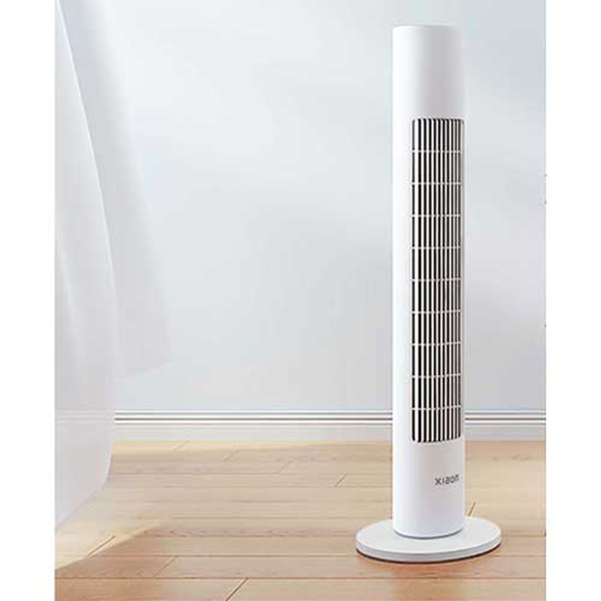 Ventilatore bianco, alto, cilindrico su un pavimento in legno vicino a un muro bianco e una tenda.