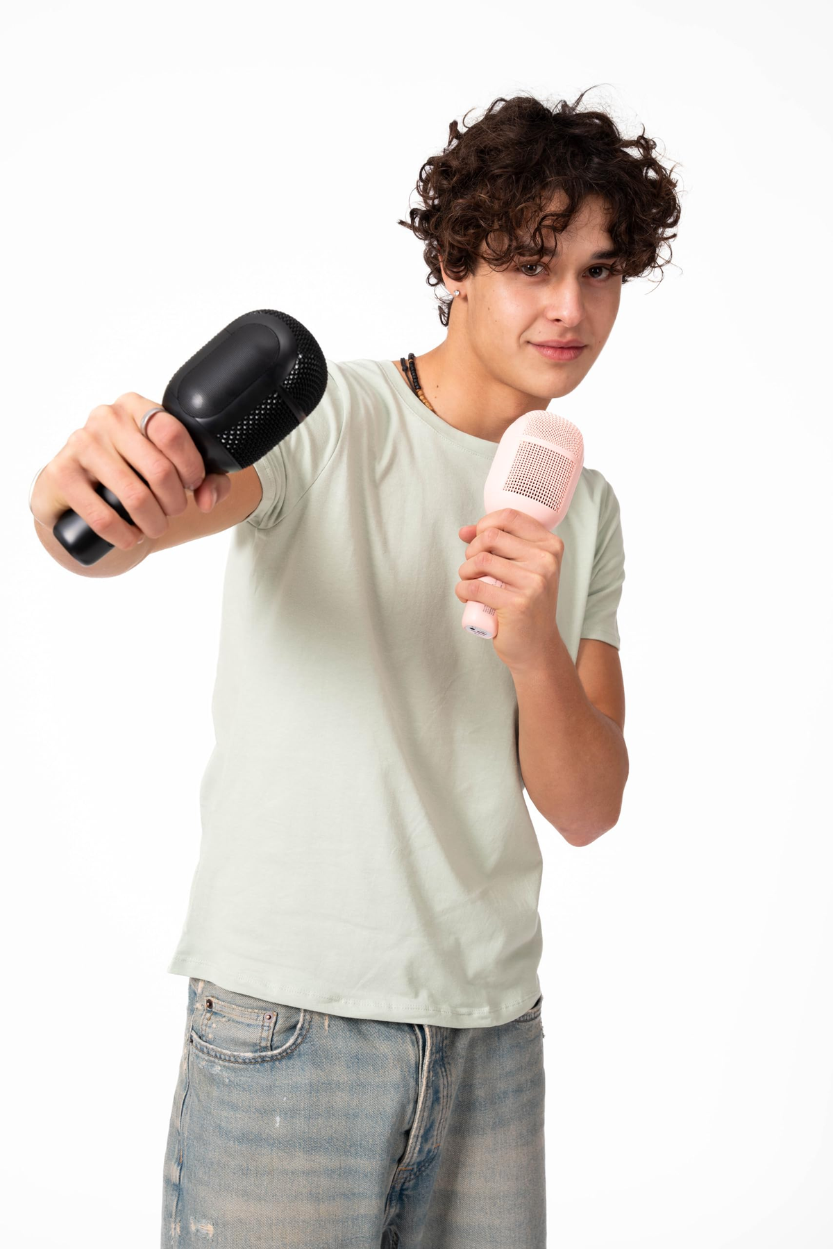 Joven sosteniendo dos micrófonos de karaoke, uno negro, otro rosa, sonriendo y mirando a la cámara.