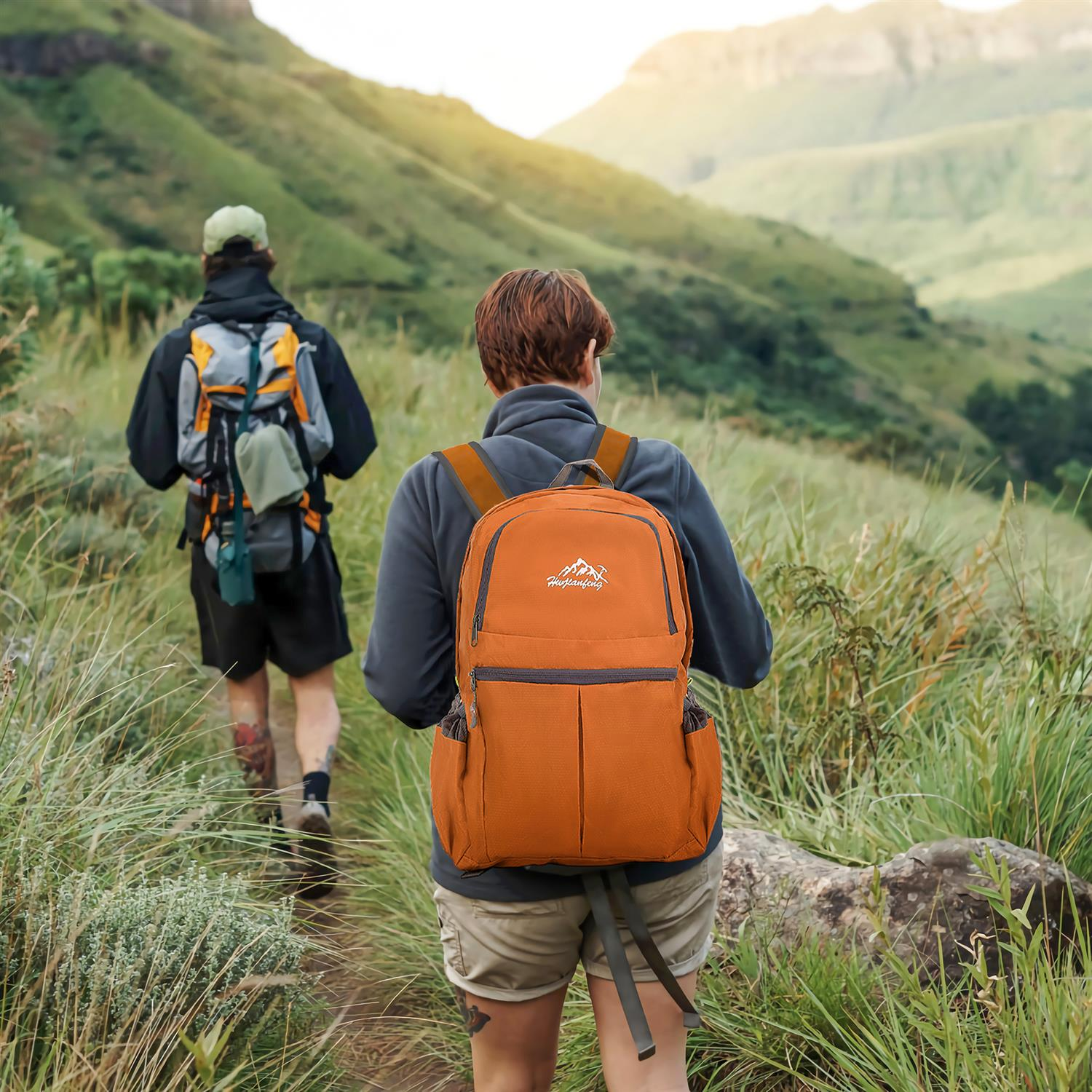 Zwei Personen wandern in den Bergen mit Rucksäcken. Einer hat einen orangen Rucksack.