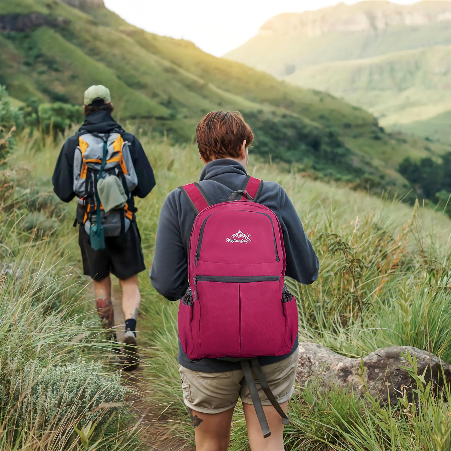Zwei Personen wandern auf einem Pfad in den Bergen, mit Rucksäcken und einem roten Rucksack im Vordergrund.