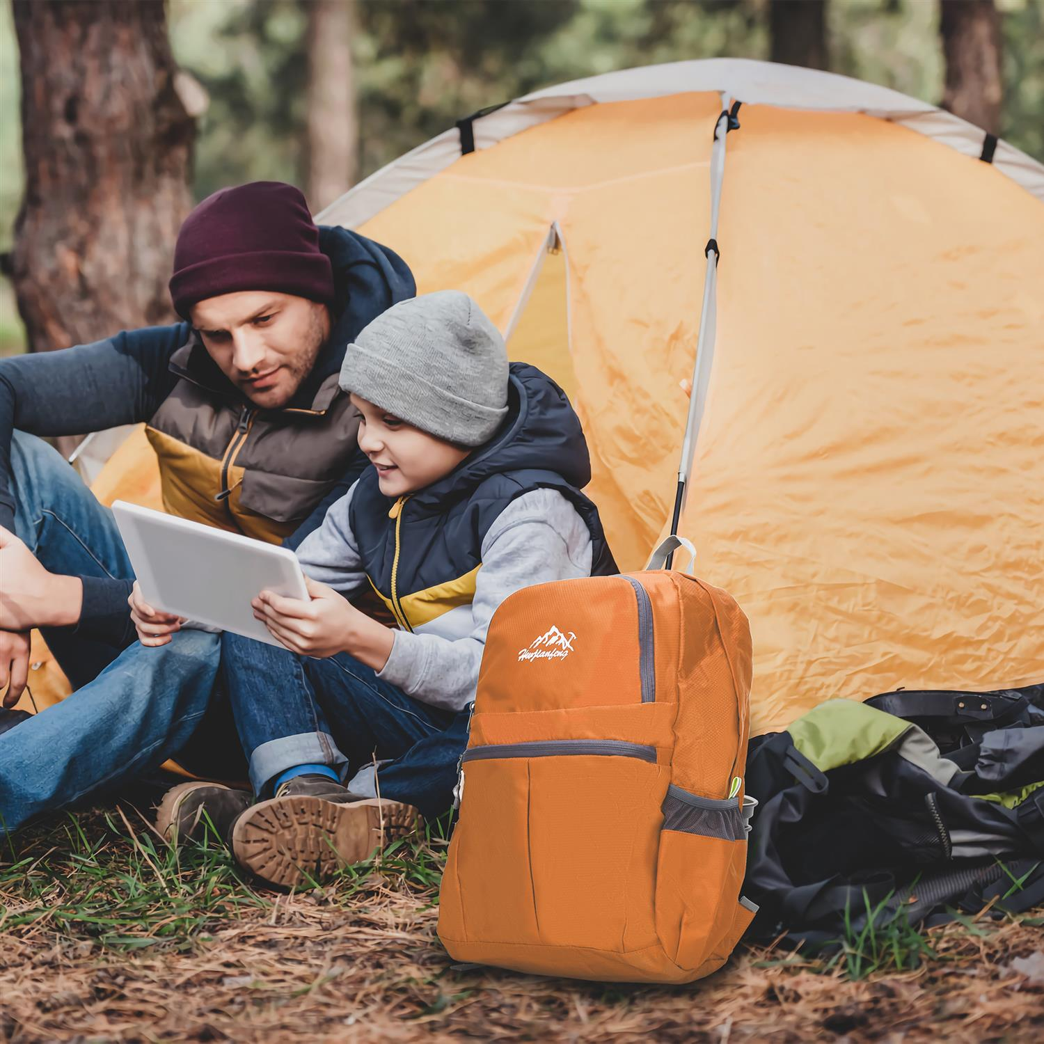 Ein Vater und Sohn betrachten ein Tablet vor einem Zelt und einem Rucksack.