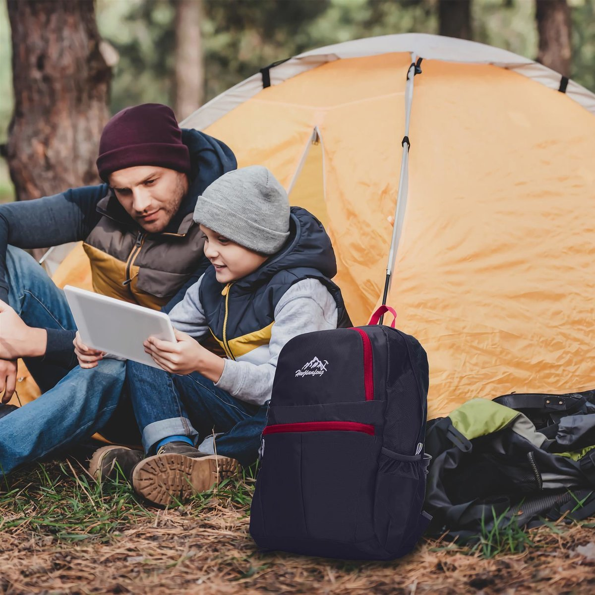 Vater und Sohn mit Tablet am Zelt, Rucksack davor.