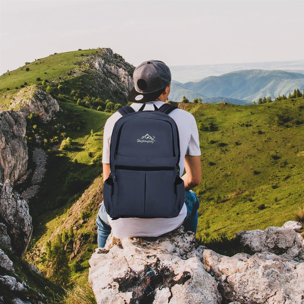 Person sitzt auf einem Felsen, blickt auf Berge mit Rucksack.