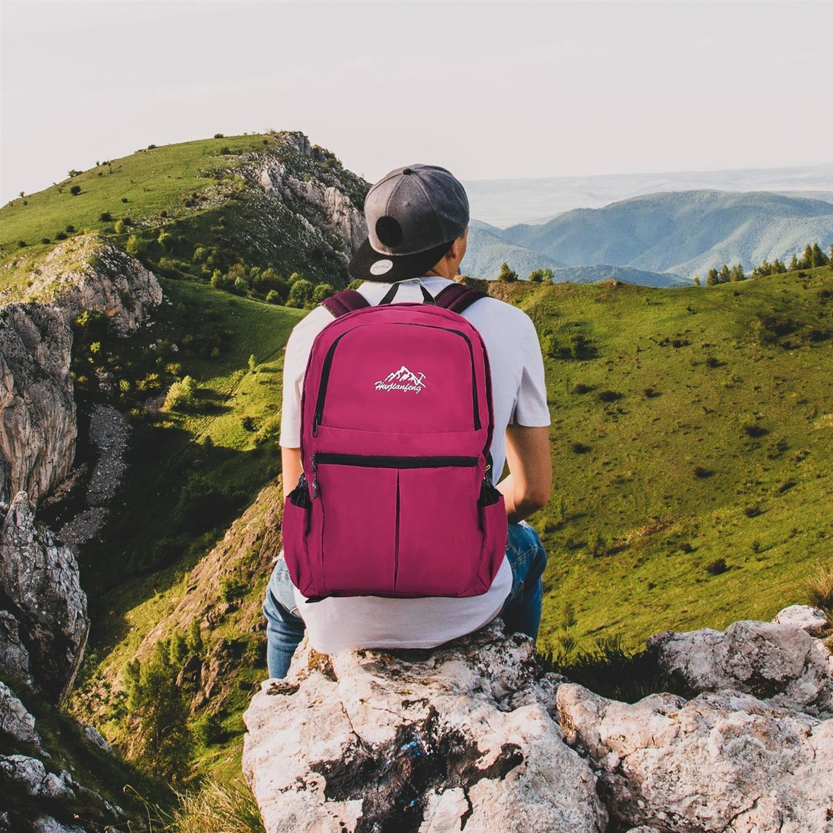 Ein Mann mit Rucksack sitzt auf einem Felsen und blickt auf eine Bergkette.