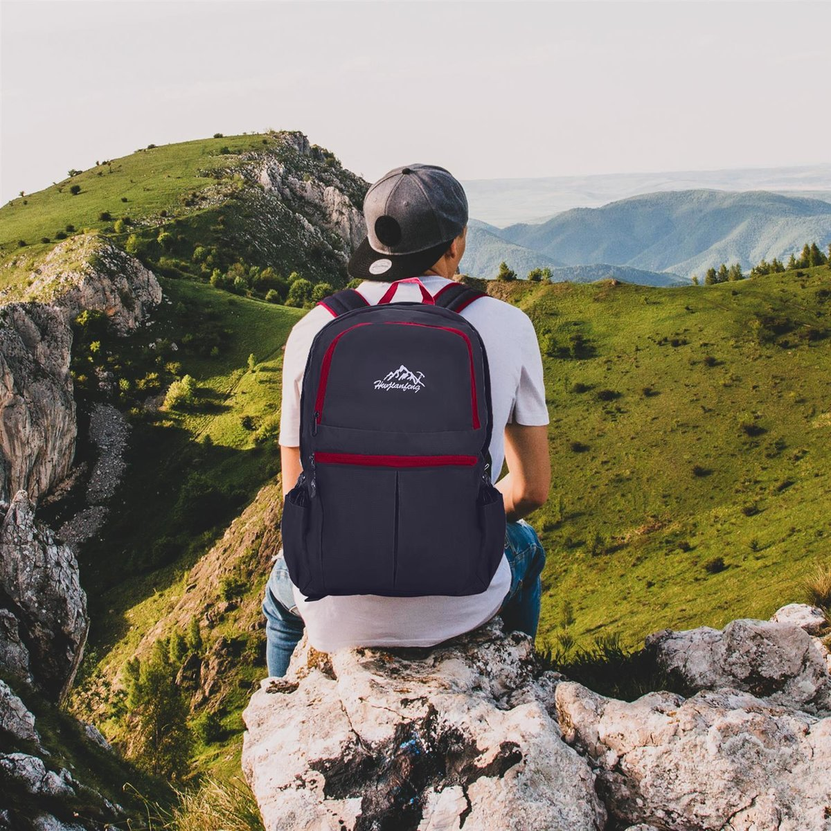 Person sitzt auf einem Felsen mit Blick auf eine Berglandschaft, trägt einen Rucksack.