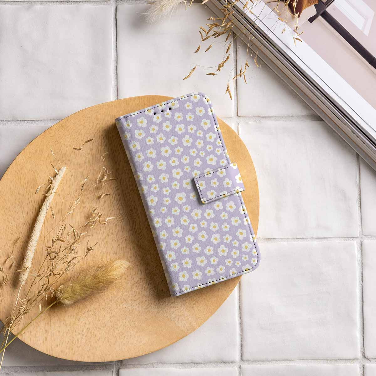 Telefoonhoesje met wit madeliefpatroon op een houten bord met decoratie.