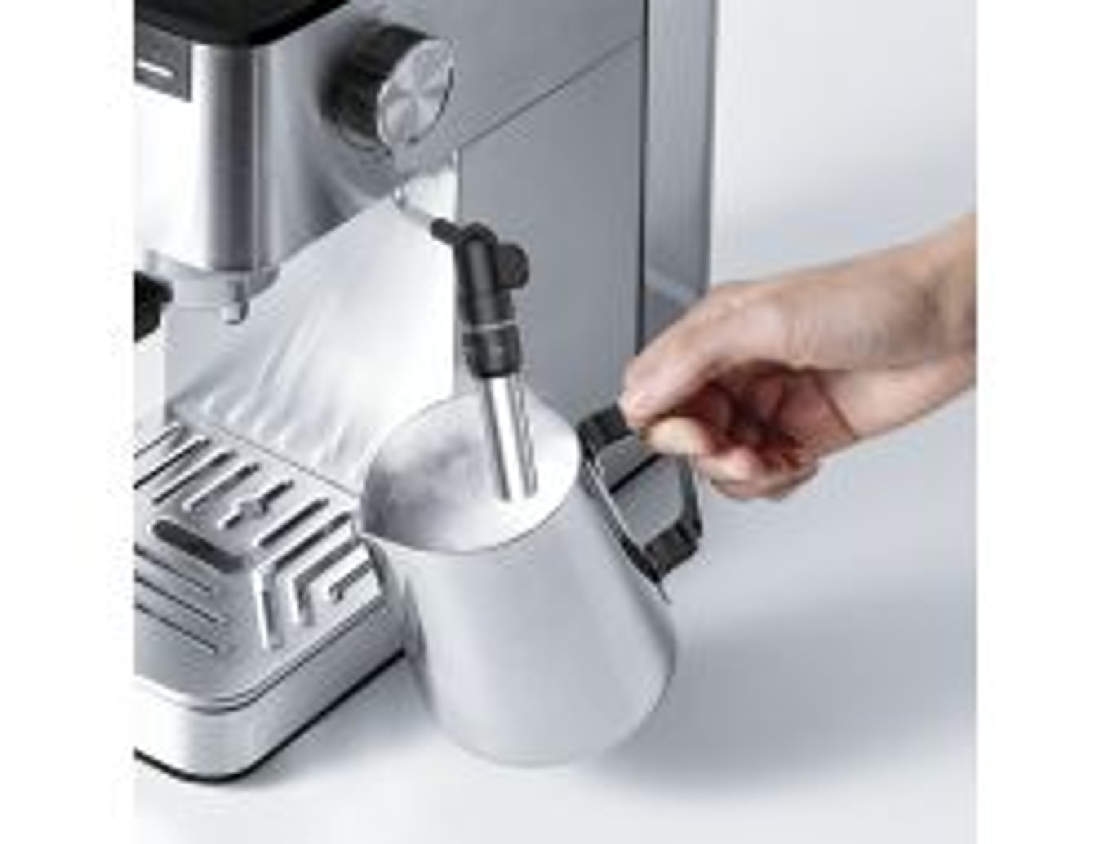 Una mano che monta il latte in un bricco di metallo usando la lancia vapore di una macchina per espresso.