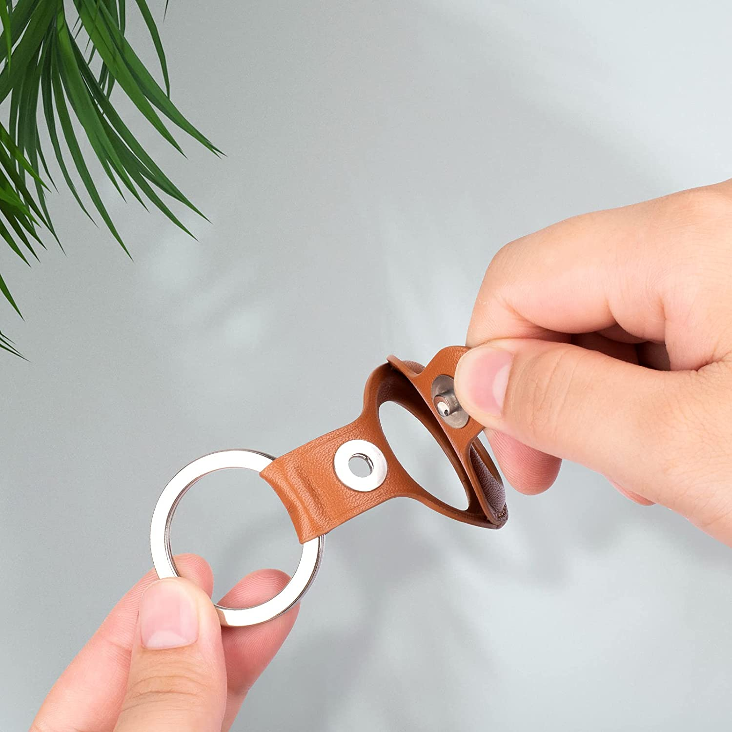 Hände einer Person, die einen braunen Leder-Schlüsselanhänger mit einem silbernen Ring zusammenbauen.
