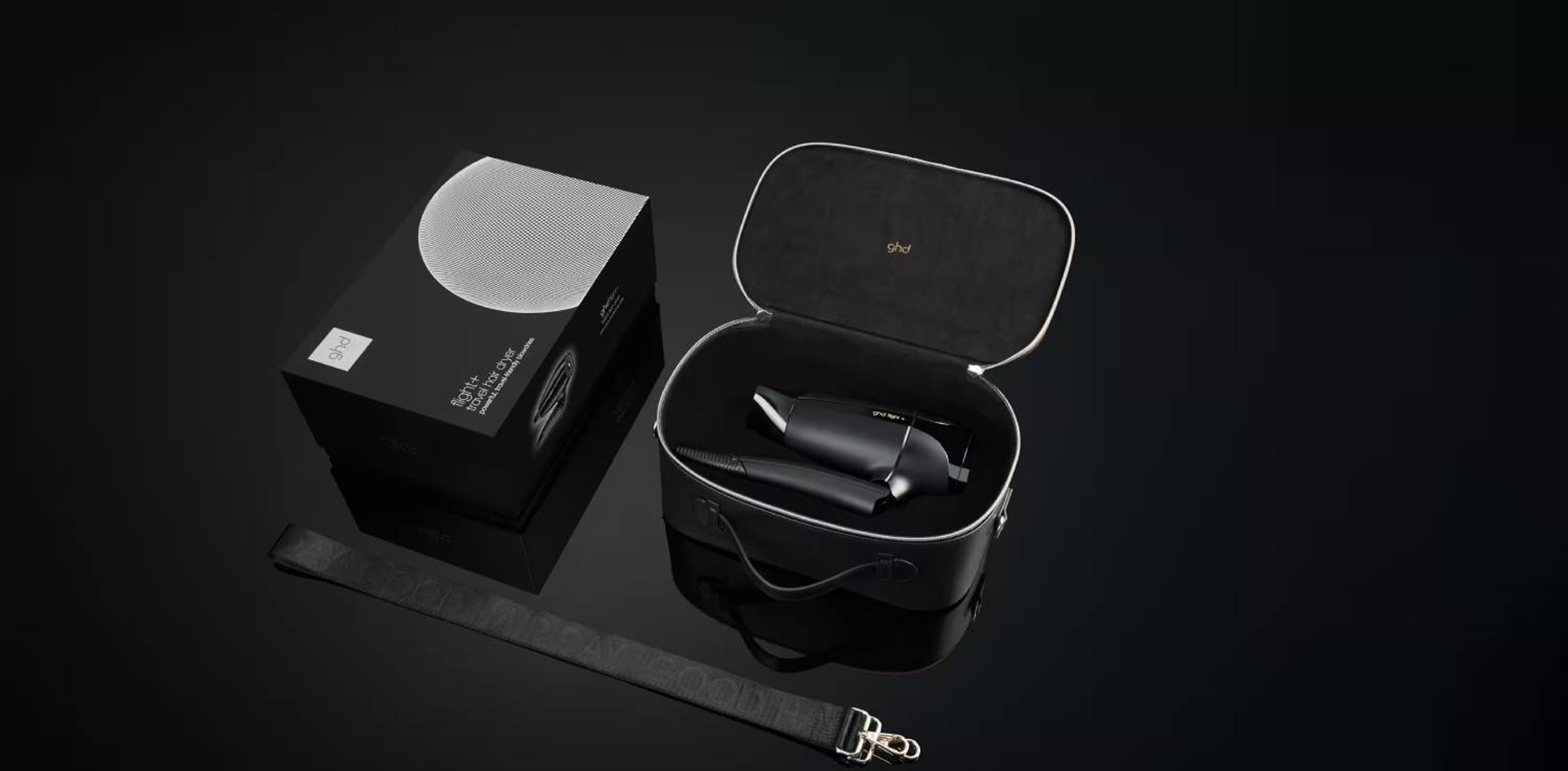 Una scatola nera e una custodia in pelle con strumenti per lo styling dei capelli all'interno, su una superficie nera.