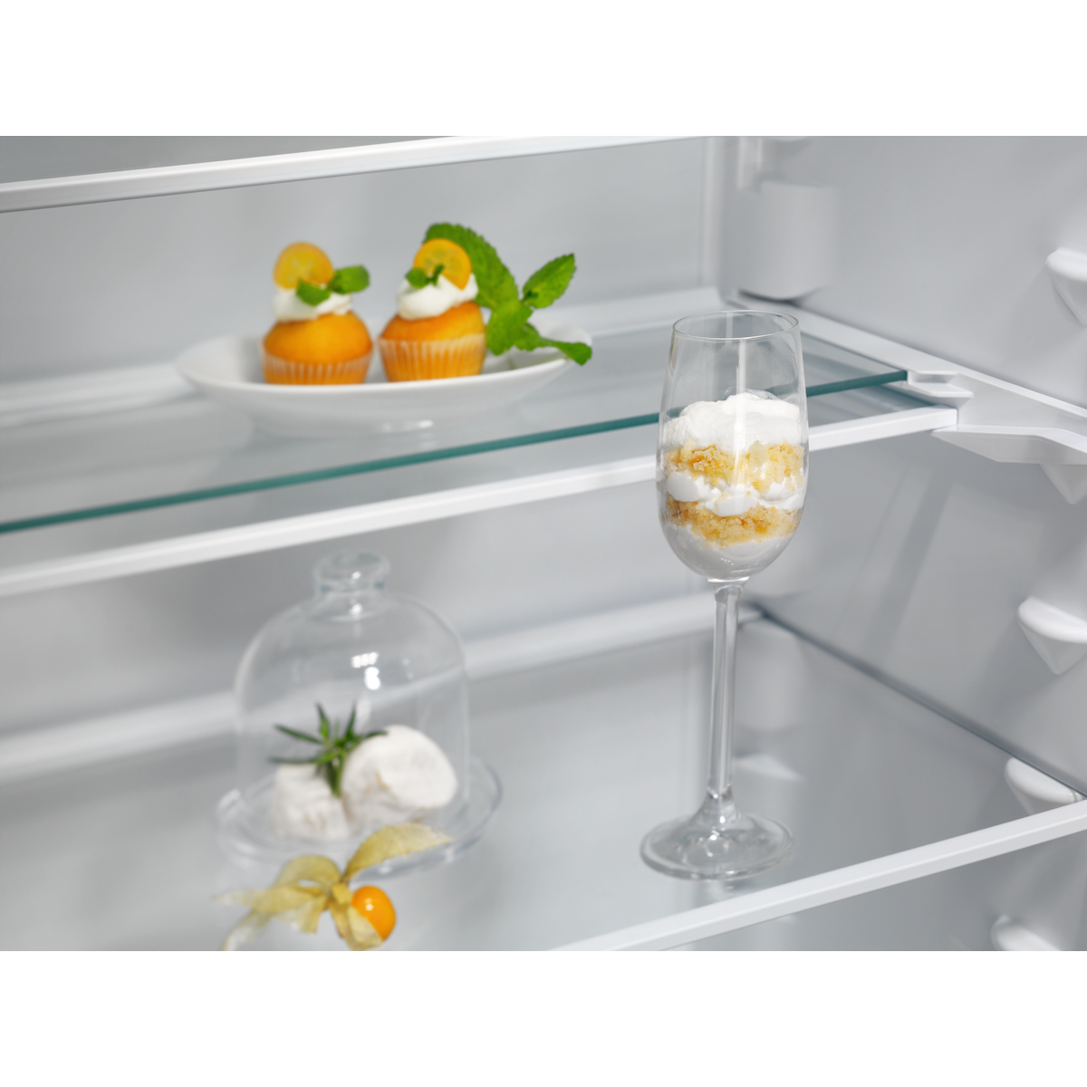 Un ripiano del frigorifero con cupcakes, un dessert in un bicchiere e una campana.