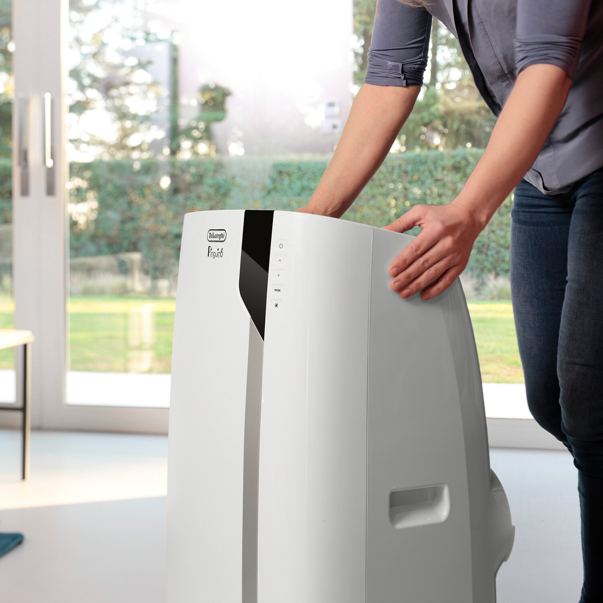 Kobieta kładzie ręce na białym klimatyzatorze. Jasne tło.