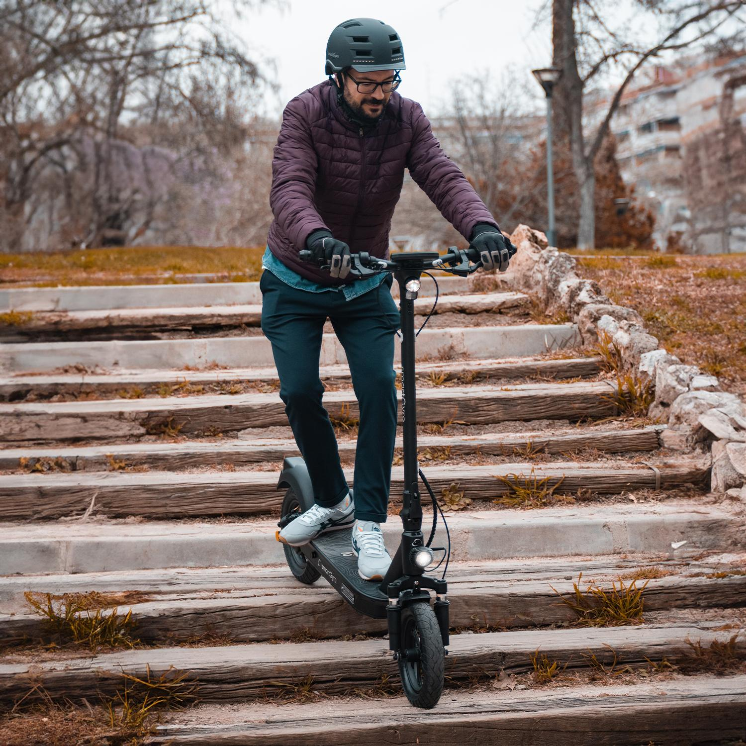 Mężczyzna jadący na hulajnodze elektrycznej po drewnianej ścieżce. Ma na sobie kask i okulary.