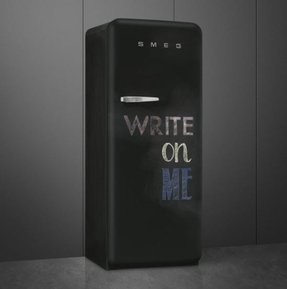 Un refrigerador SMEG negro con las palabras 'WRITE on ME' en letras coloridas.