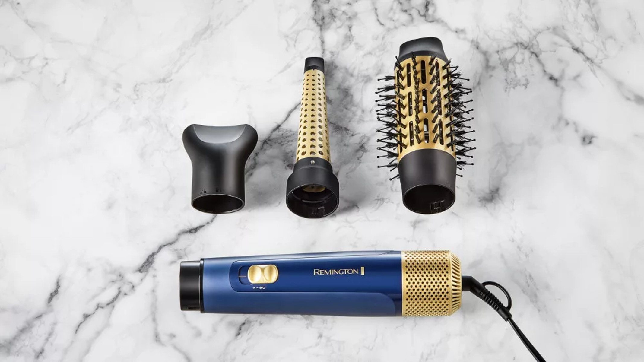 Set per lo styling dei capelli: asciugacapelli e tre accessori. Colori oro e nero, su superficie in marmo.