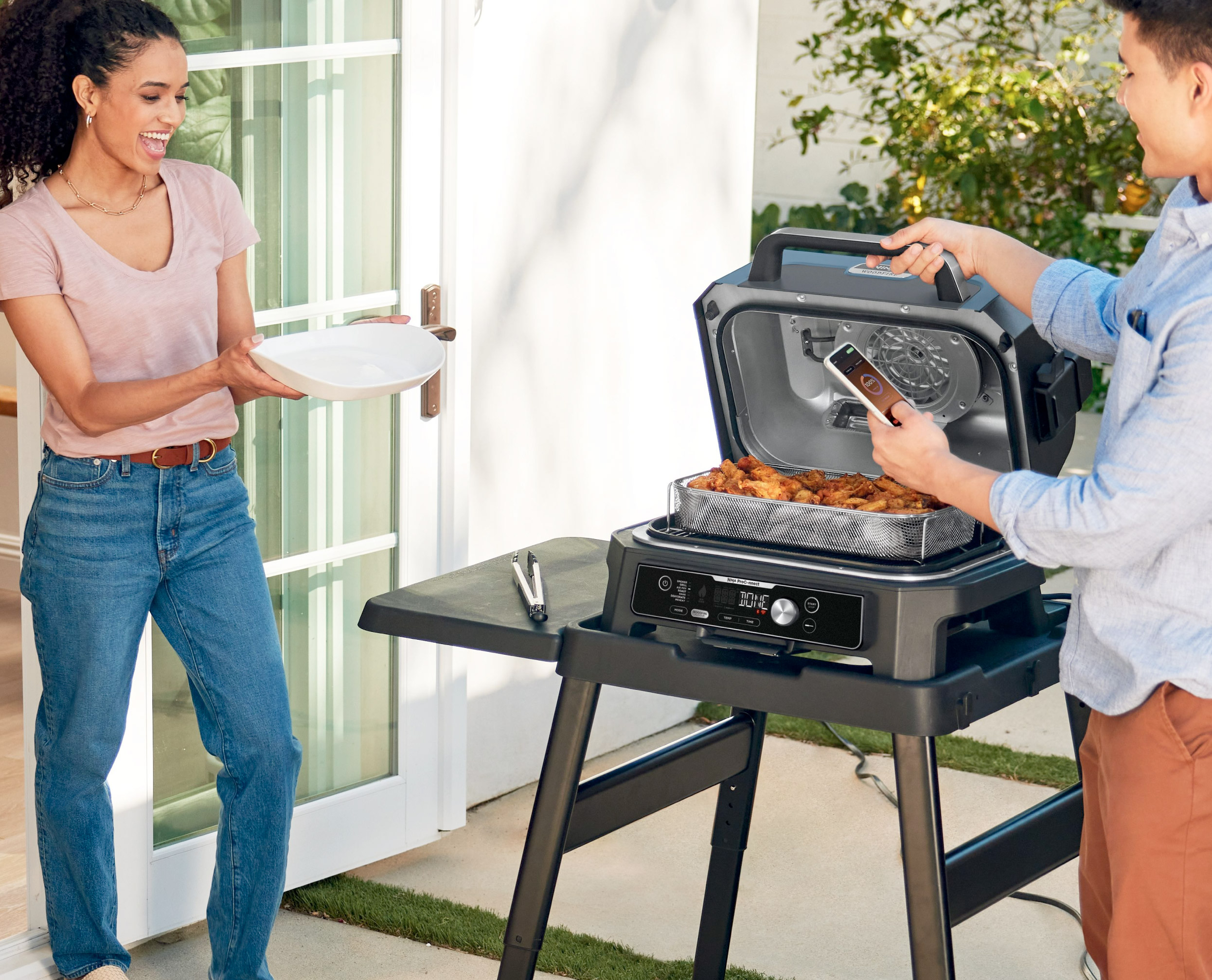 Twee mensen die buiten grillen. Een vrouw houdt een bord vast, een man gebruikt een grill.