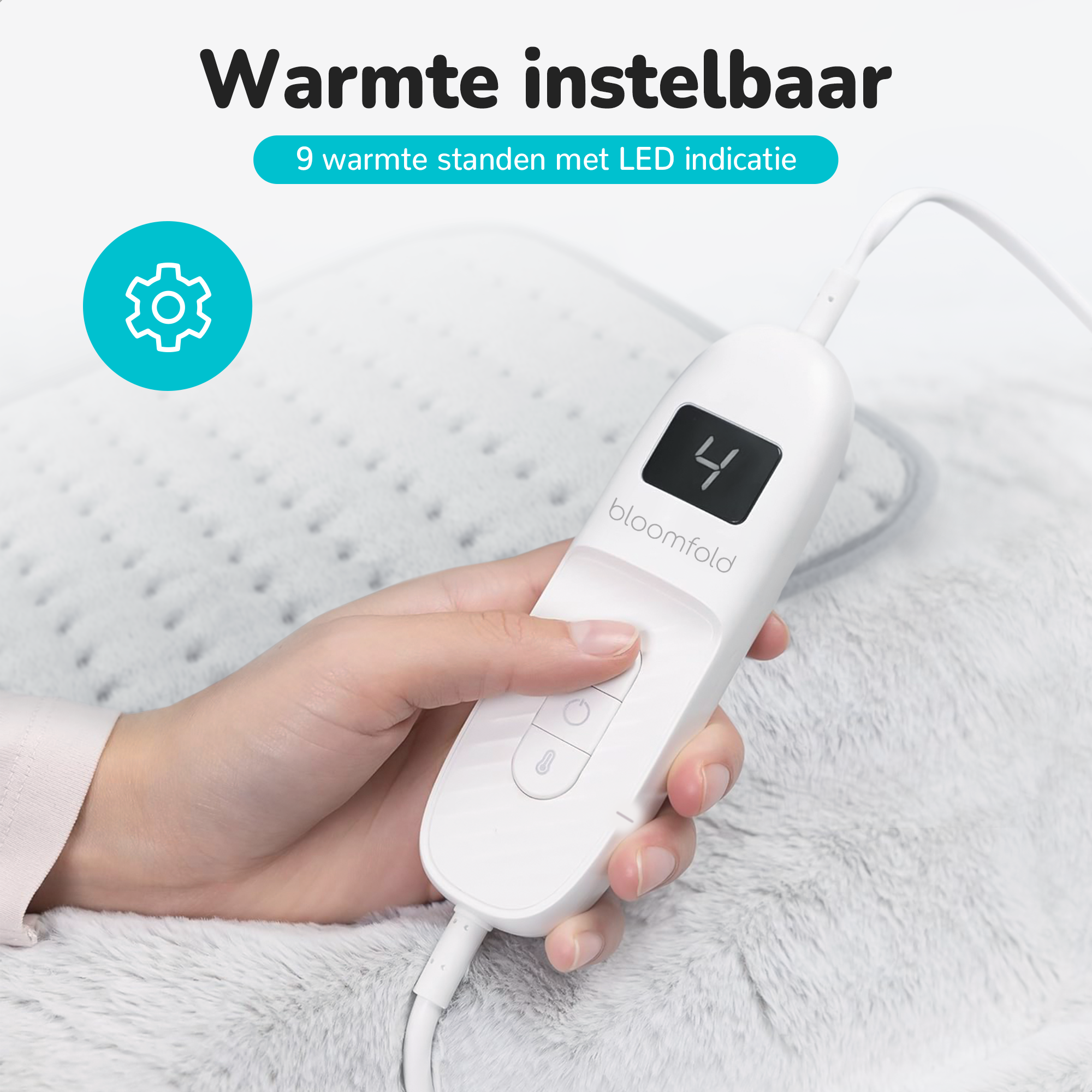 A hand holding a white heating pad controller. Display shows number 4. The pad is on a gray blanket.