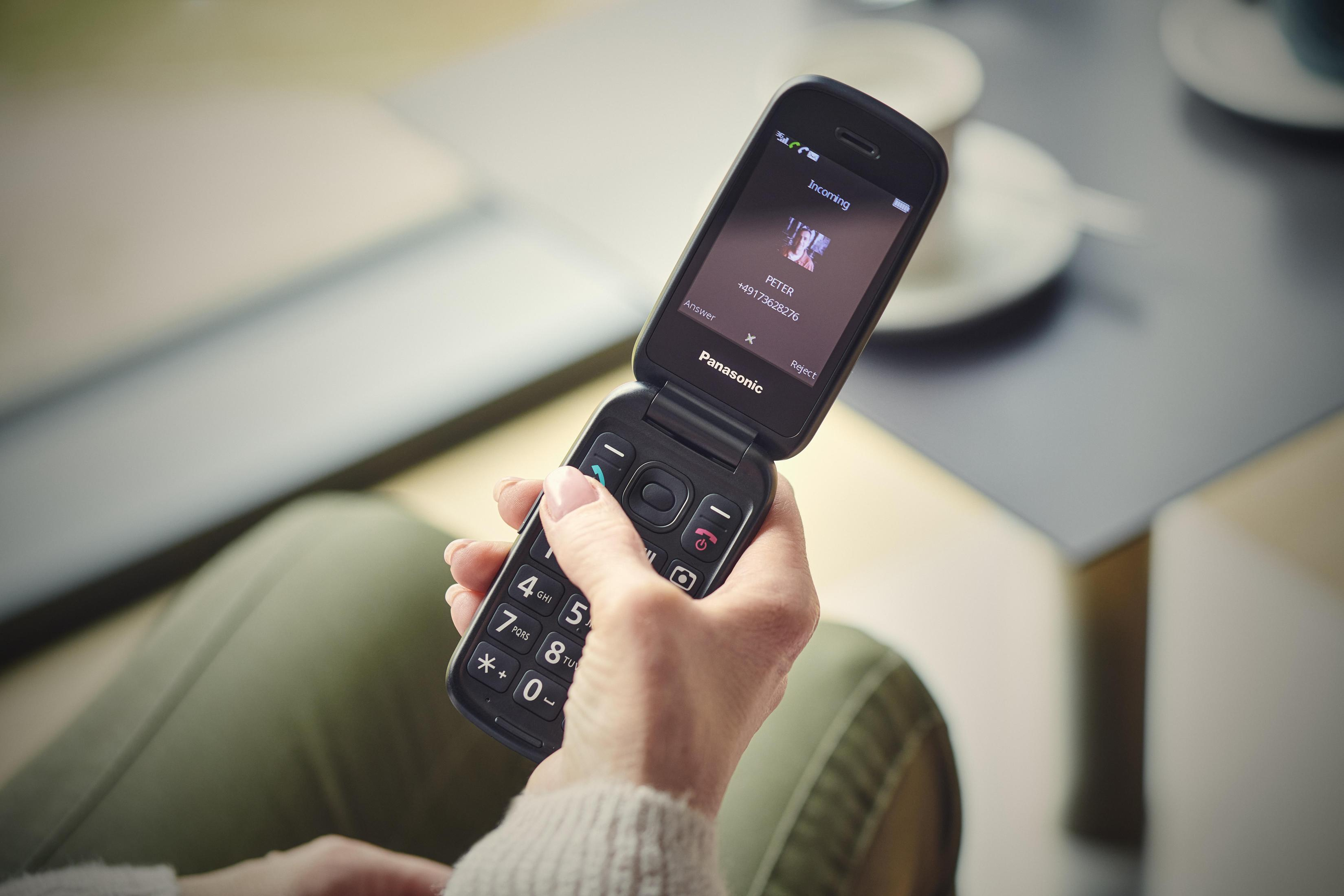 A flip phone is held and open, displaying an incoming call.