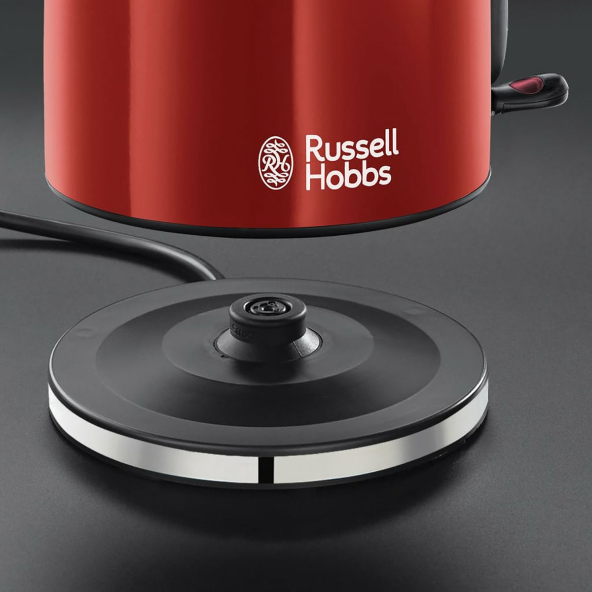 Czerwony czajnik Russell Hobbs na czarnej podstawie. Podstawa ma srebrne obramowanie.