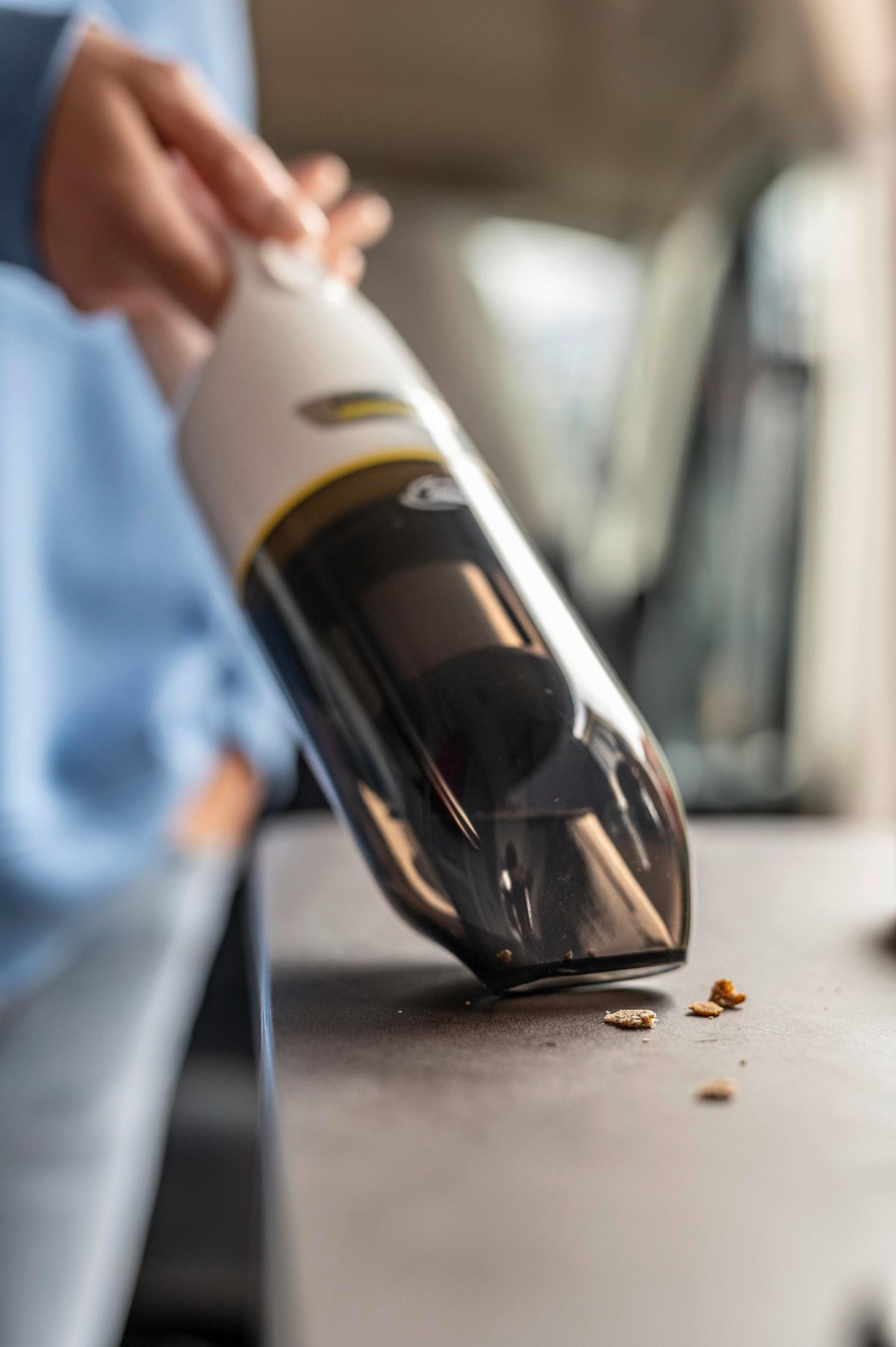 Une personne utilisant un aspirateur à main blanc et noir sur une surface.