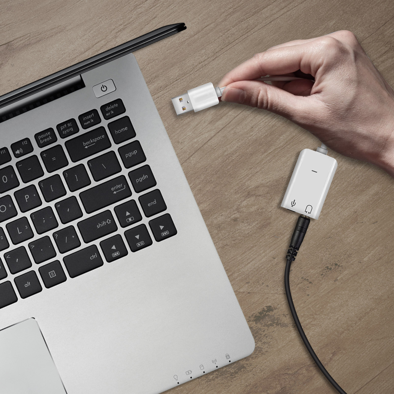 Una persona tiene un adattatore USB-C bianco vicino a un laptop su un tavolo di legno.