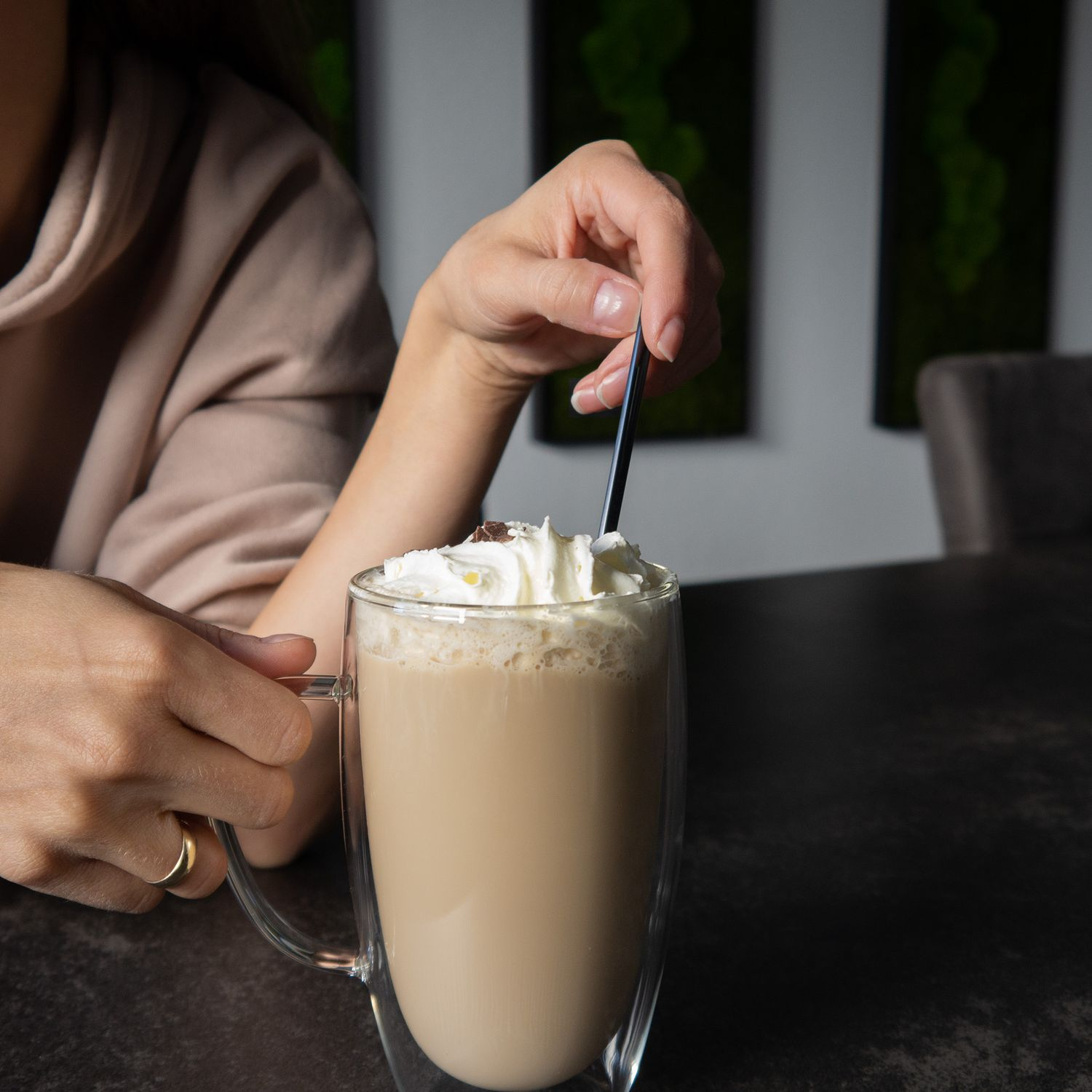 Eine Person rührt Schlagsahne in einem Kaffeebecher auf einem dunklen Tisch um.