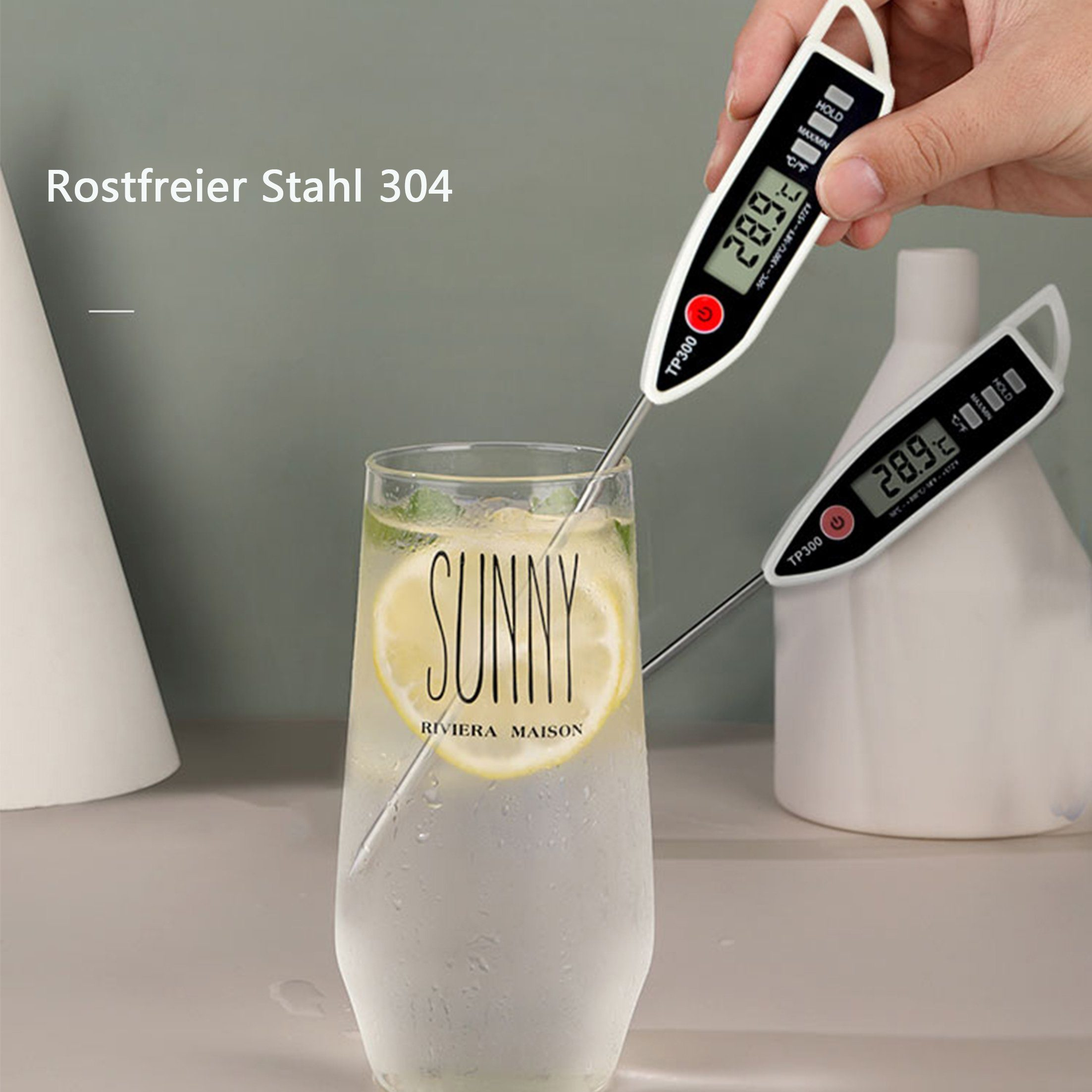 Zwei Thermometer in einem Glas mit Zitronengetränk. Eines wird gehalten, das andere ist im Glas.