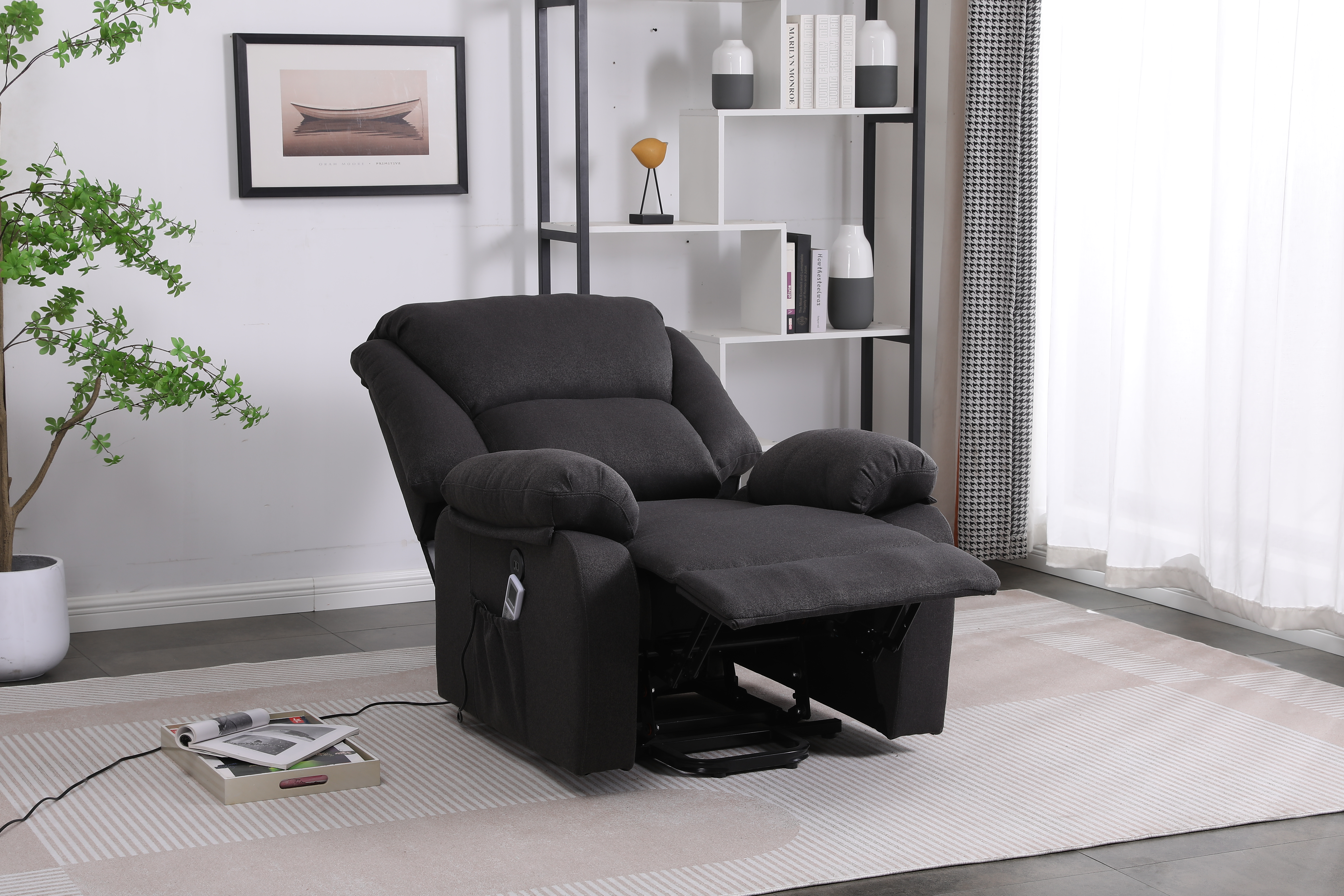 Sillón reclinable gris oscuro con mesa auxiliar con libros y mando a distancia, y una estantería negra en el fondo.