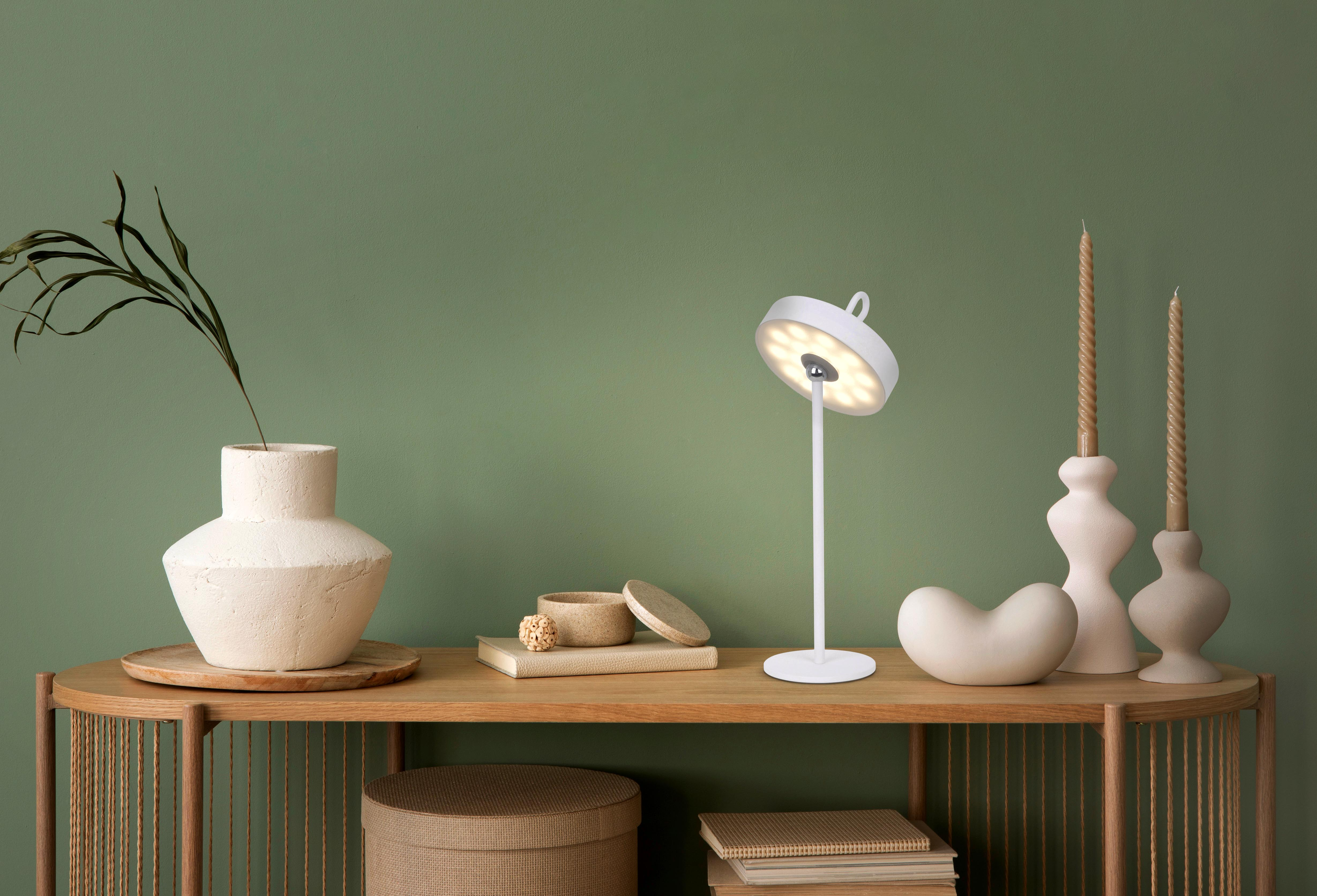 Weiße Lampe auf einem Holztisch, mit Kerzen und einer Vase. Grüne Wand im Hintergrund.