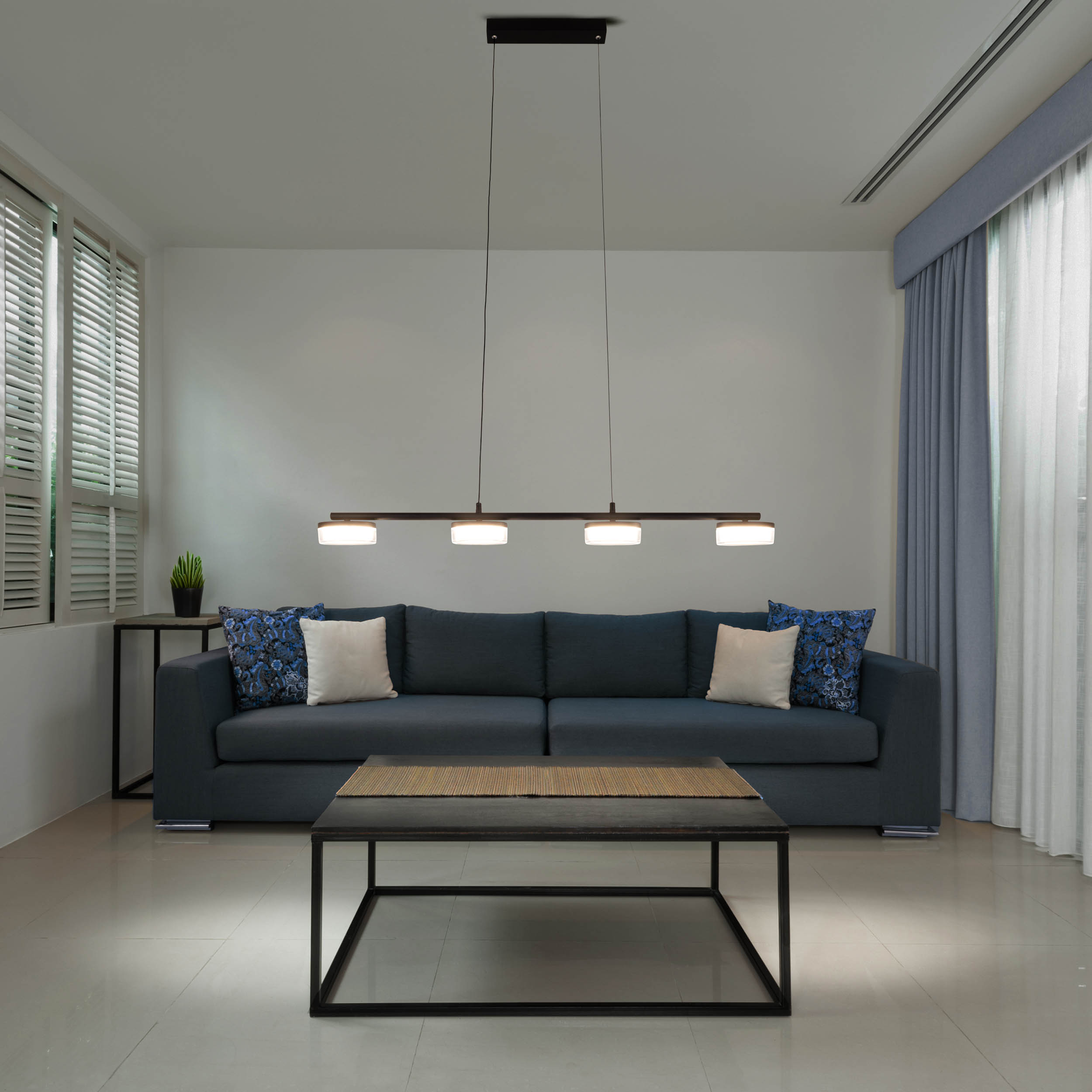 Ein modernes Wohnzimmer mit dunkelblauem Sofa, Kissen, Couchtisch und Pendelleuchte.