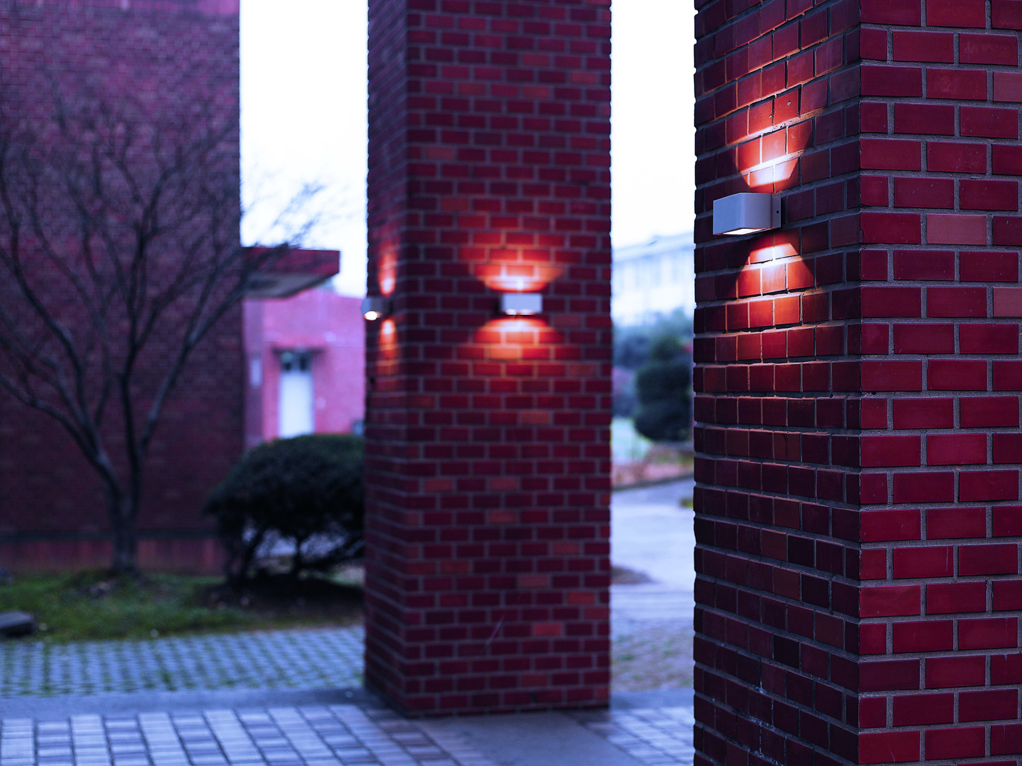 Zwei Backsteinsäulen mit montierten Lichtern. Im Hintergrund ist ein Baum. Lichter scheinen auf die Ziegel.