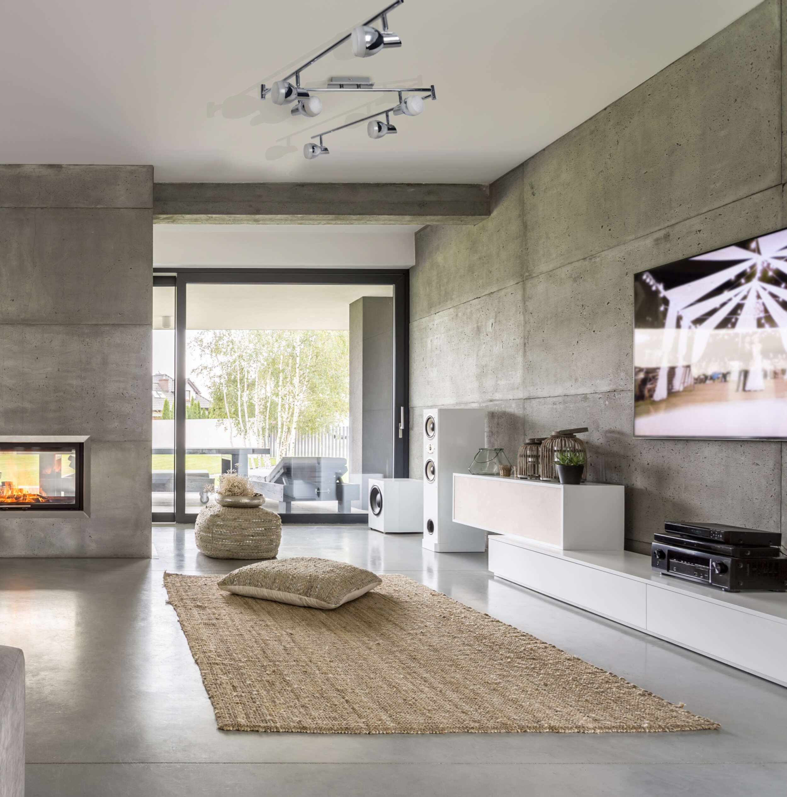 Modernes Wohnzimmer mit Betonwand und Teppich. Der Raum hat einen Kamin und einen Fernseher. Die Leuchte ist sichtbar.