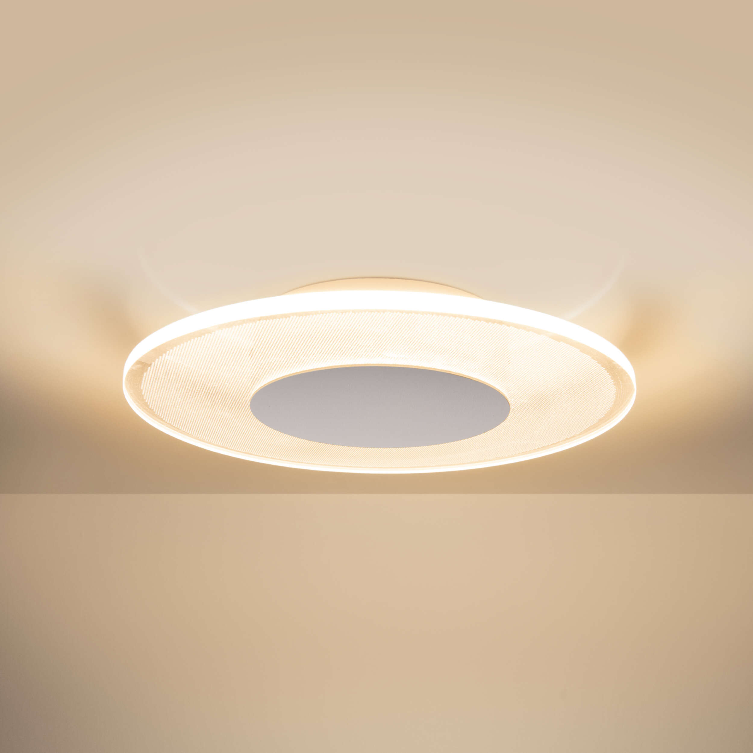 Eine kreisförmige Deckenleuchte. Das Licht hat einen weißen Außenring und einen grauen Innenkreis. Der Hintergrund ist beige.