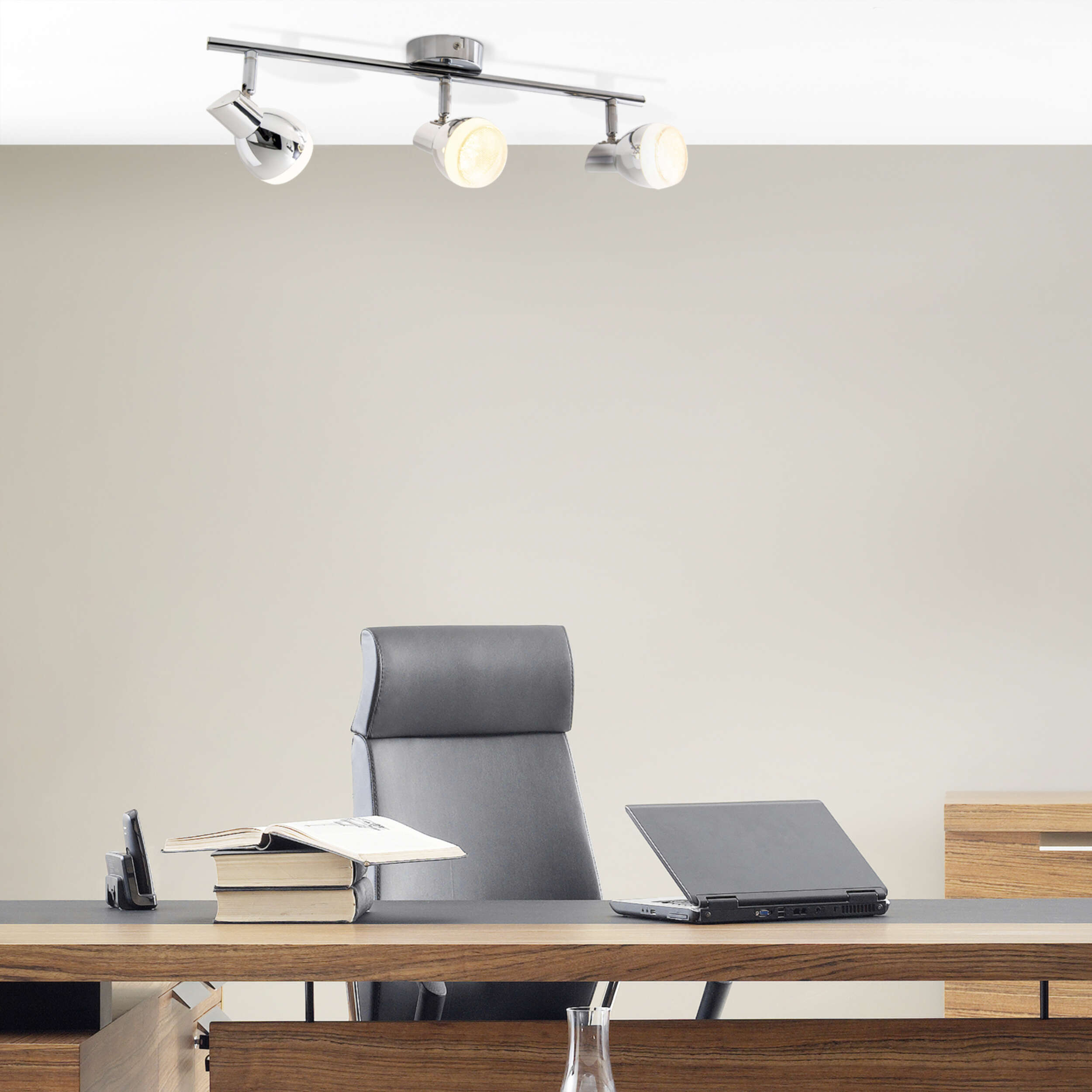 Büroszene mit Strahlern an der Decke. Schreibtisch, Stuhl und geöffneter Laptop. Beige Wände.