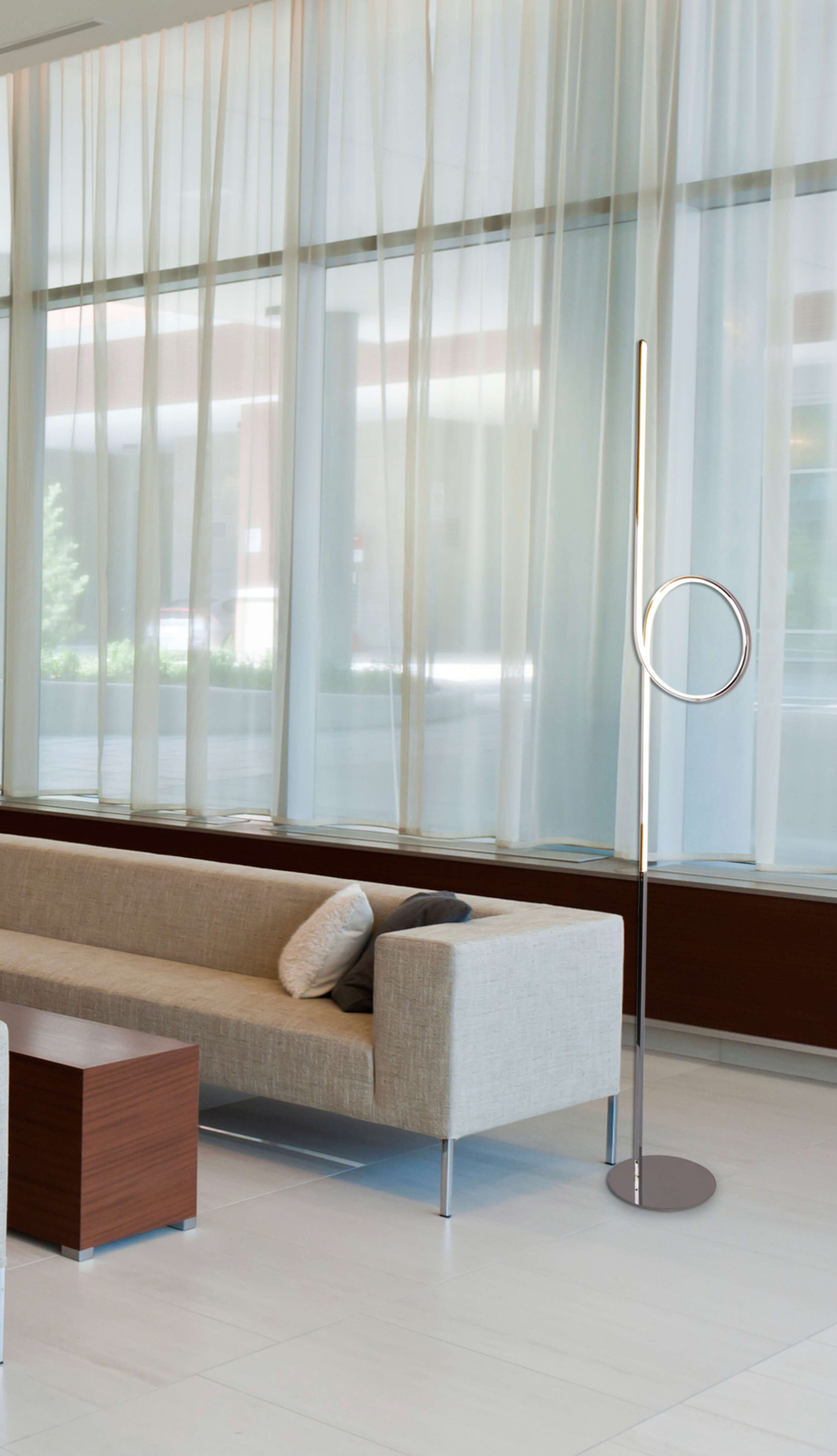 Moderne Stehlampe mit kreisförmiger Spitze, in hellem Innenraum mit Sofa und transparenten Vorhängen.