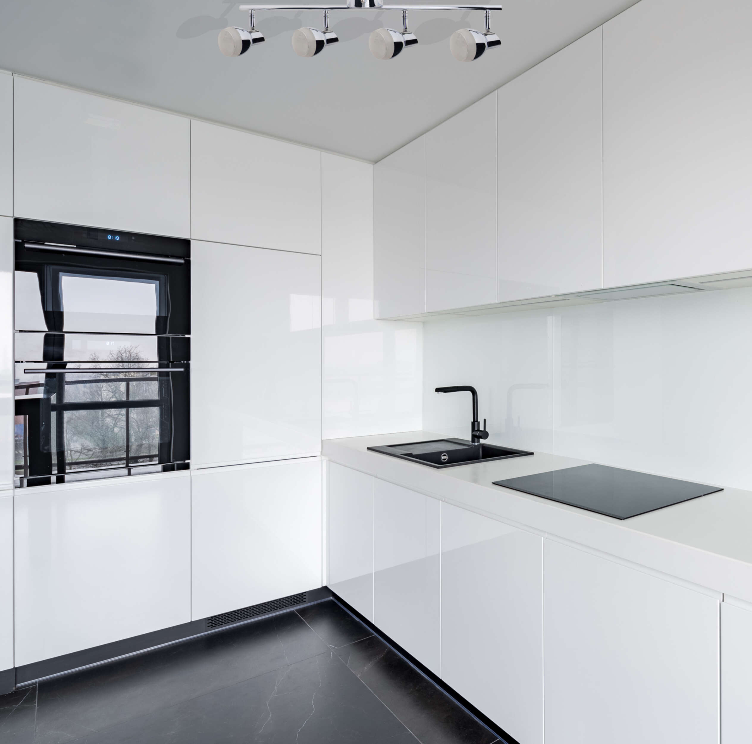 Moderne weiße Küche mit schwarzem Backofen, Spüle und Kochfeld sowie Chrom-Spots.